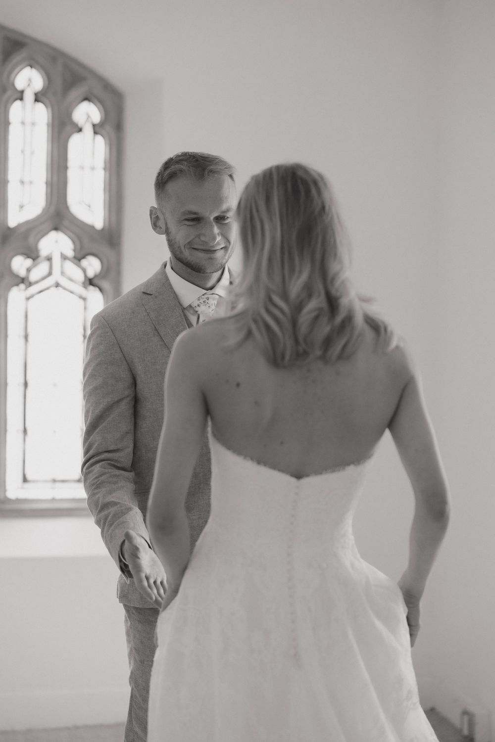 A couple sharing a tender moment during their first look in a bright church room with gothic windows in a church in Kansas City, Ks.