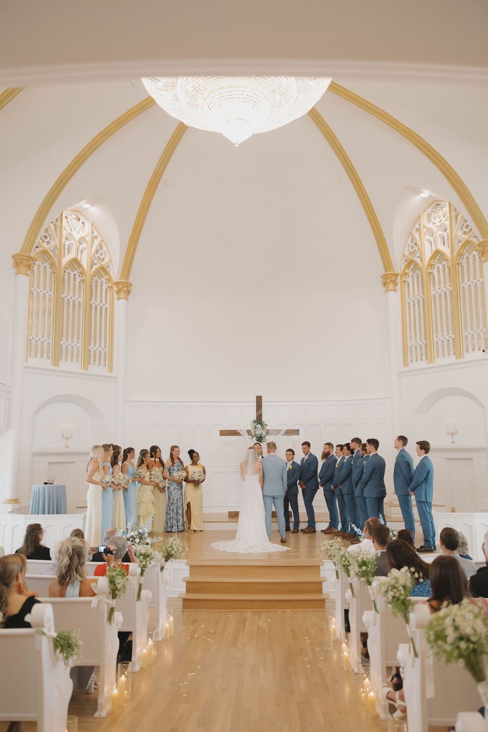 Kansas City wedding ceremony in a white chapel with golden arches, where bridal party and groomsmen stand at altar with floral decorations.