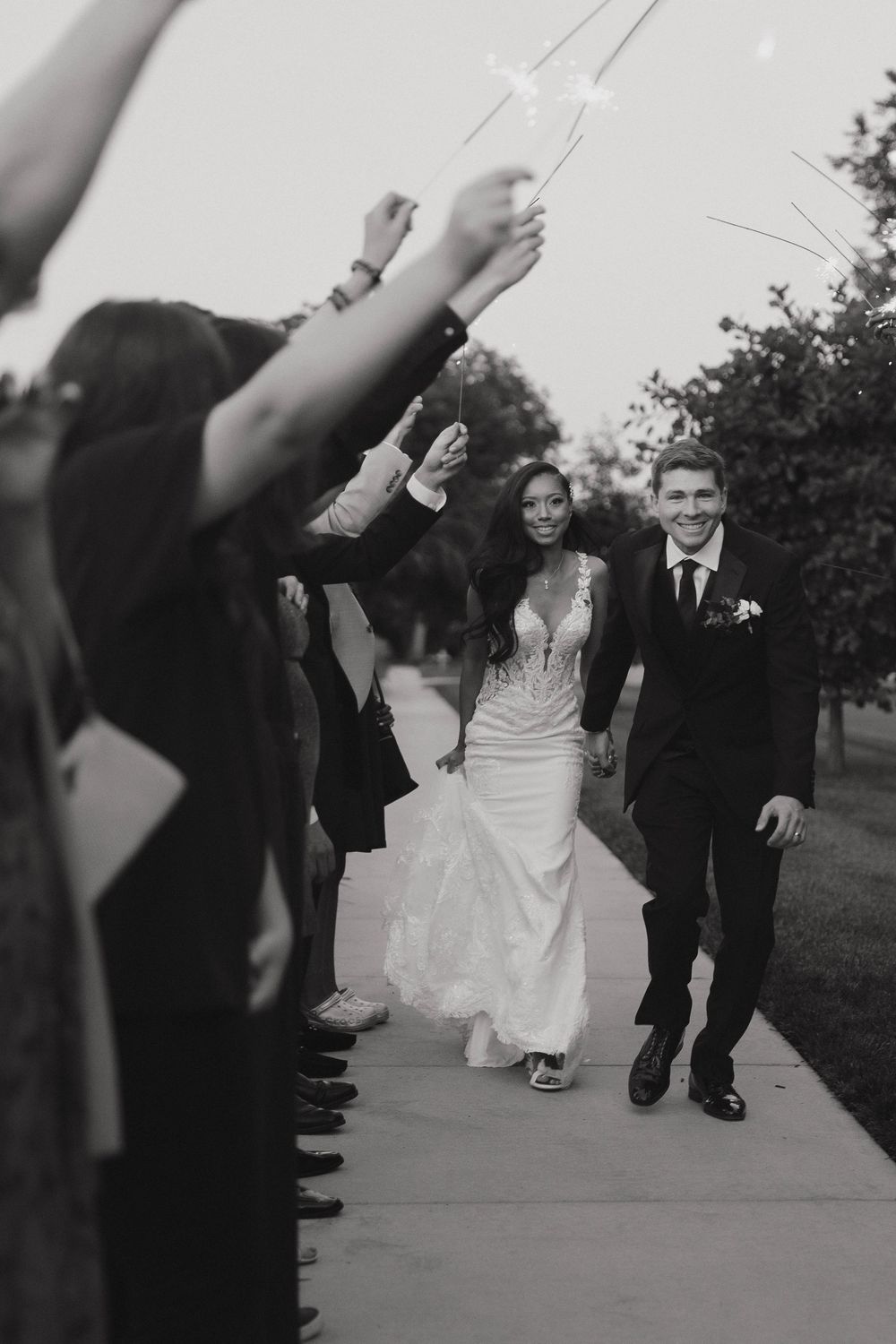 Wedding couple walks down path lined with guests holding sparklers during evening exit celebration.