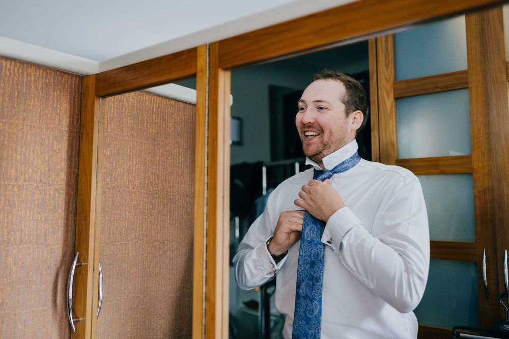 A person in a white dress shirt and blue tie adjusts their sleeve cuff while preparing for a formal event.