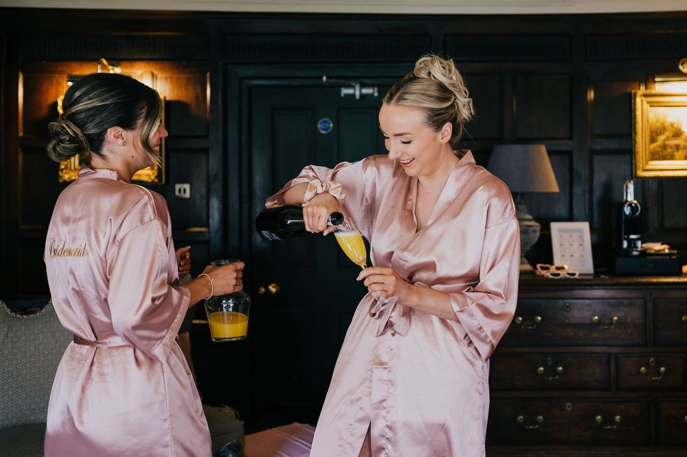 Two people in pink silk robes sharing drinks and laughing during a celebratory moment in a dark room.