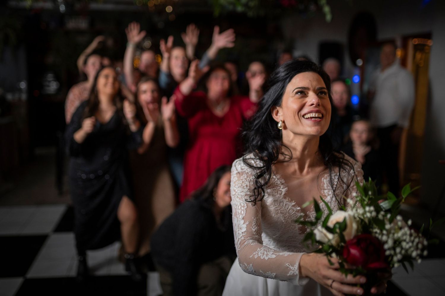A joyful bride clutches a bouquet while celebrating with excited guests during the wedding reception.