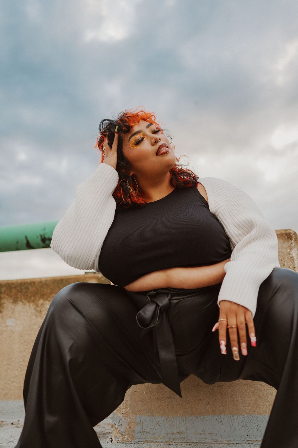 A person with red hair wearing black and white loungewear poses outdoors against a cloudy sky.