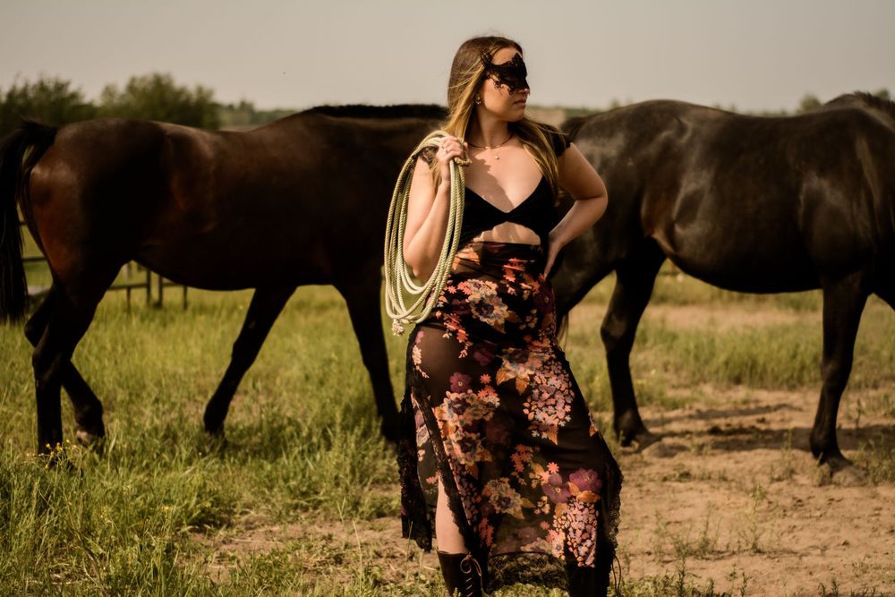 A person in a floral dress stands with a rope while horses graze in the background.
