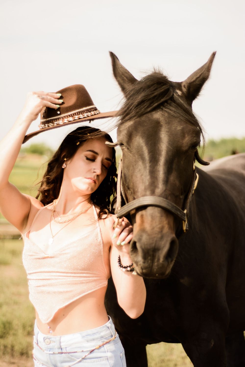 A woman in a peach top interacts affectionately with a dark horse against a light background.