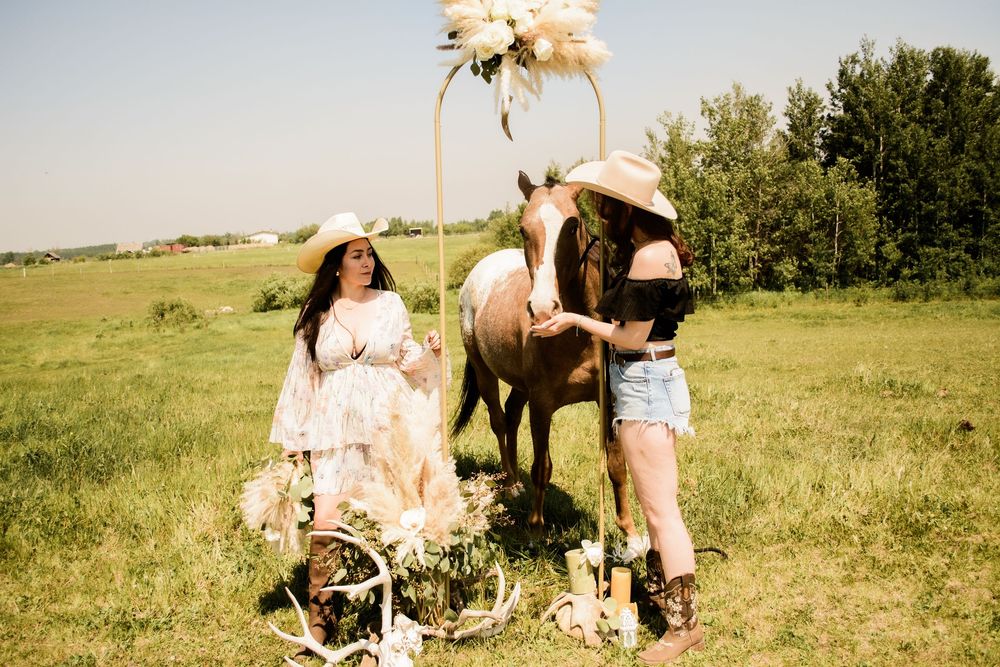 Several people and horses gather in a sunny field with trees in the background.