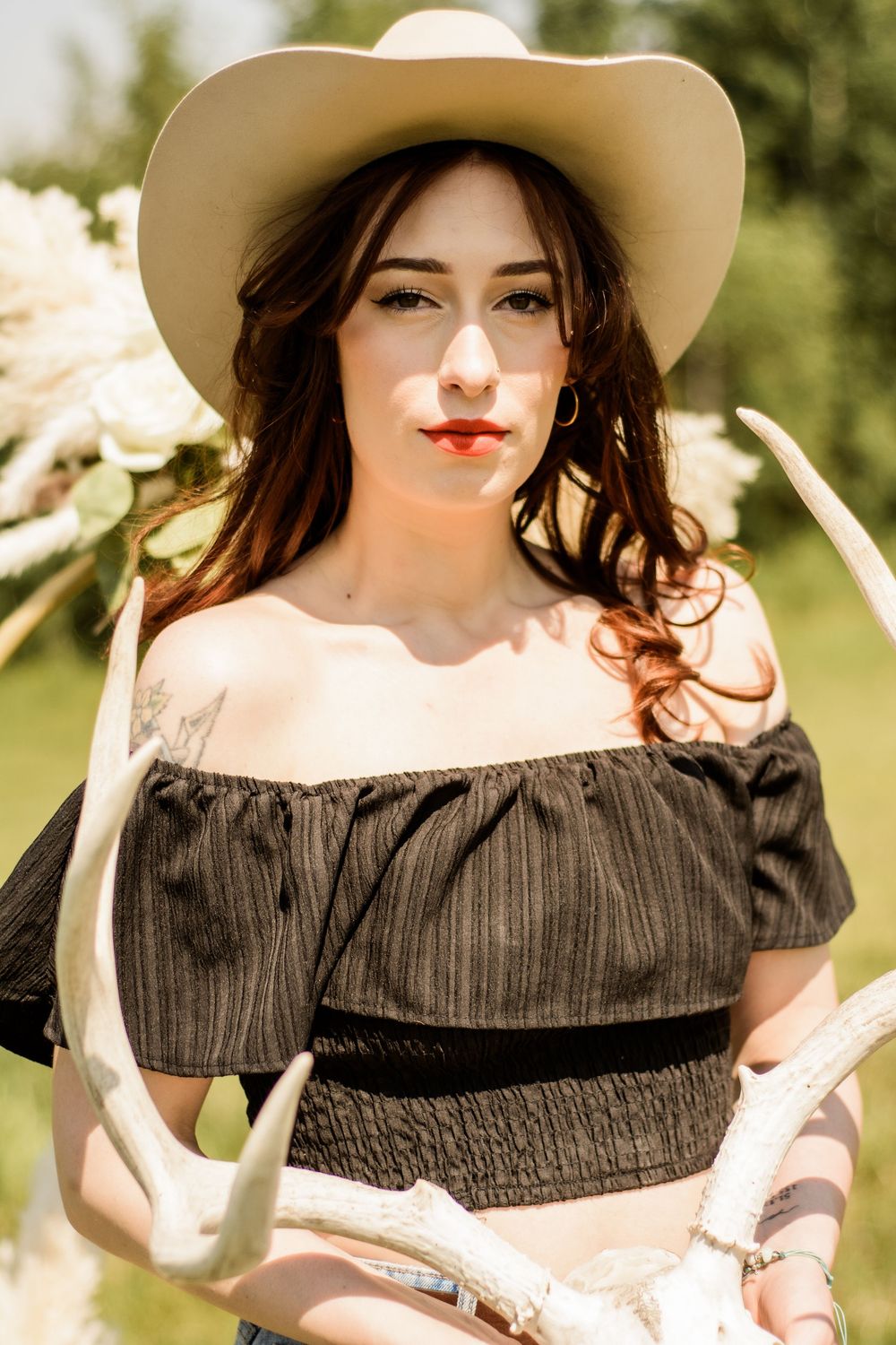 Person in western-style dress and cream cowboy hat poses amid white flowers in sunlight.