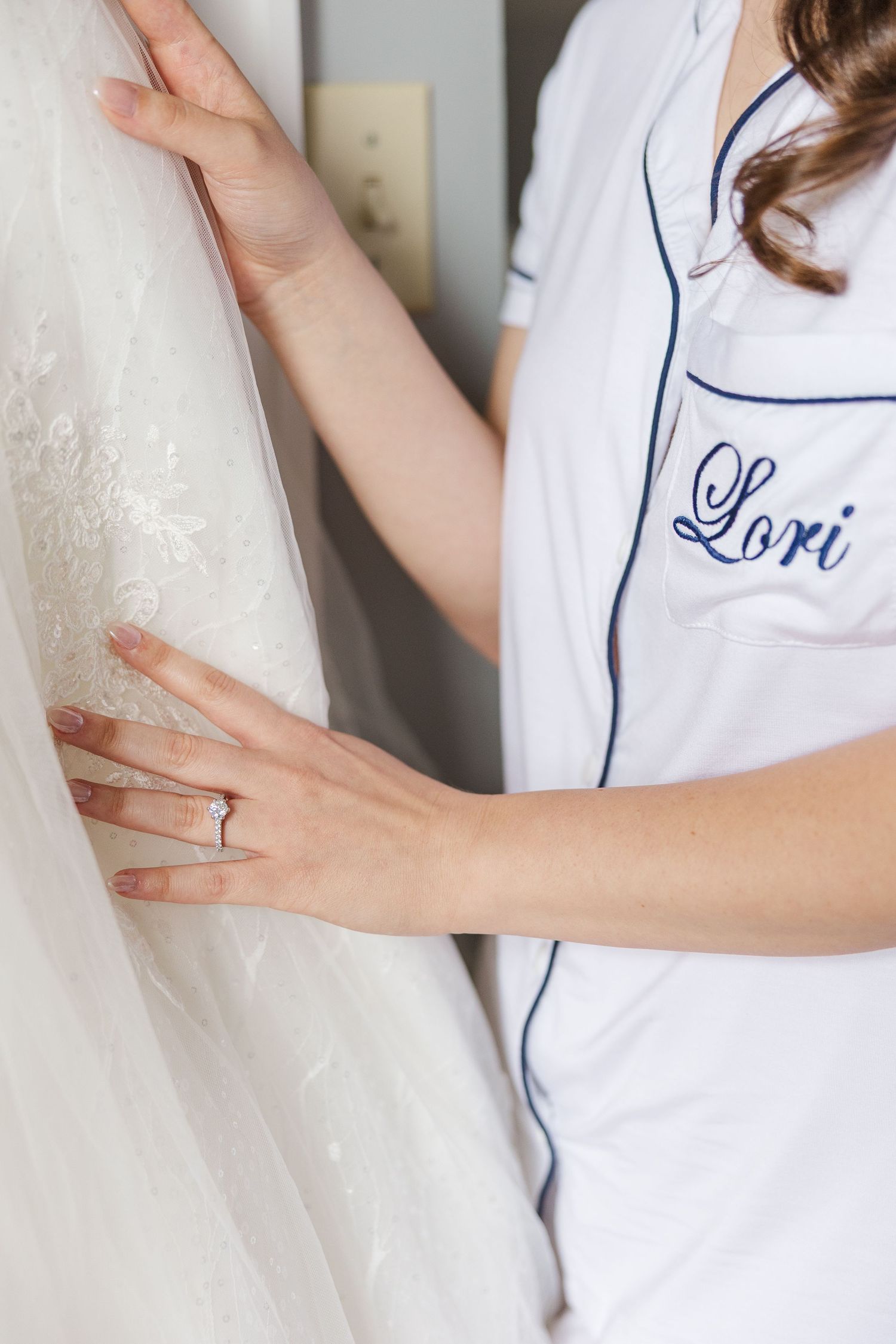 Close up of hands touching a wedding dress with person wearing monogrammed white robe with blue trim that says Lori.