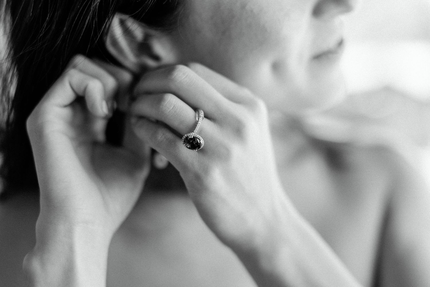 Close-up black and white photo of hands adjusting an elegant engagement ring.