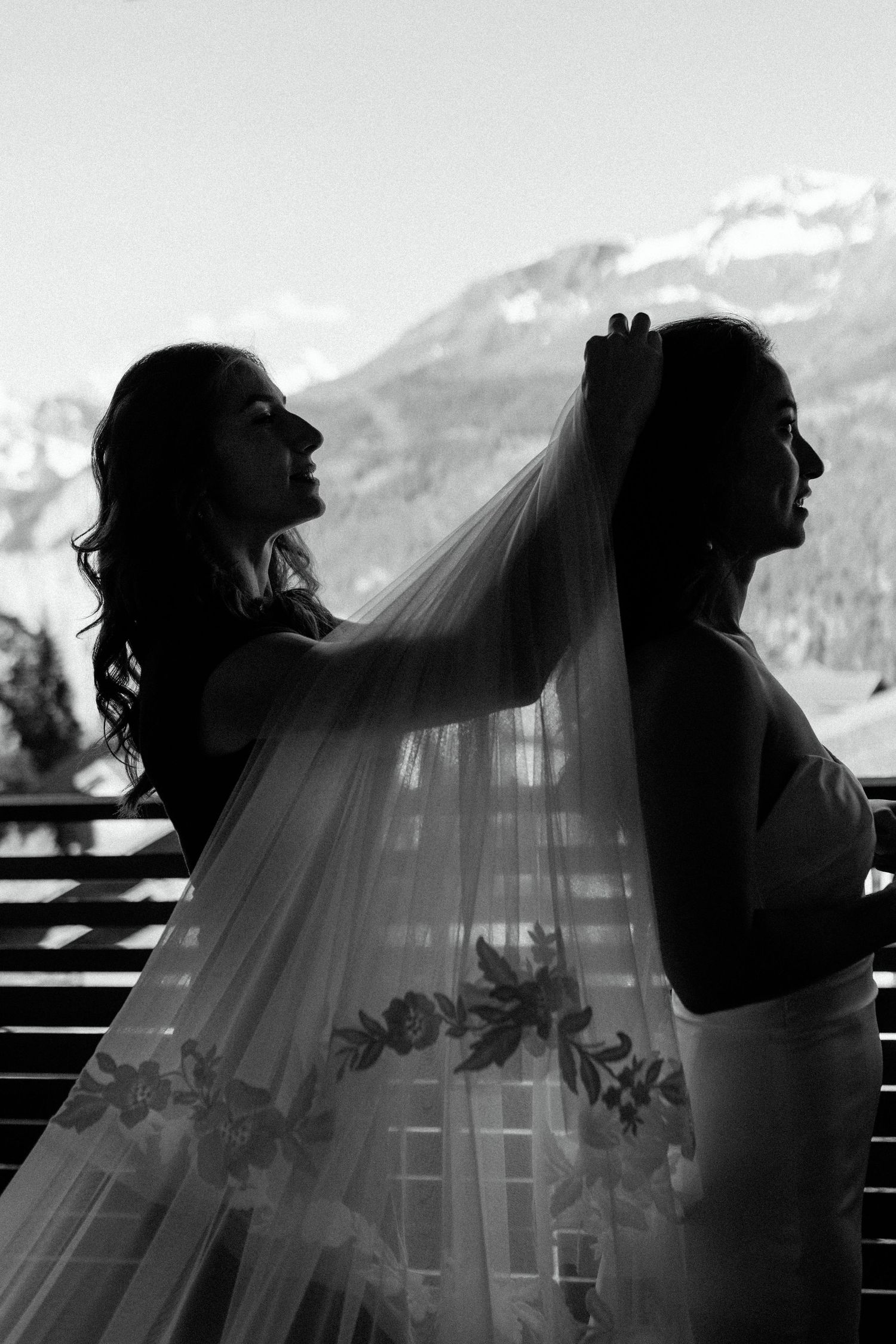 A silhouetted wedding scene with a bride's veil being adjusted before a mountain backdrop.