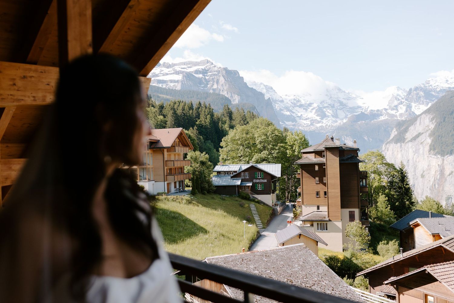 Scenic view of snow-capped Alps and traditional chalets from a wooden balcony in Switzerland.