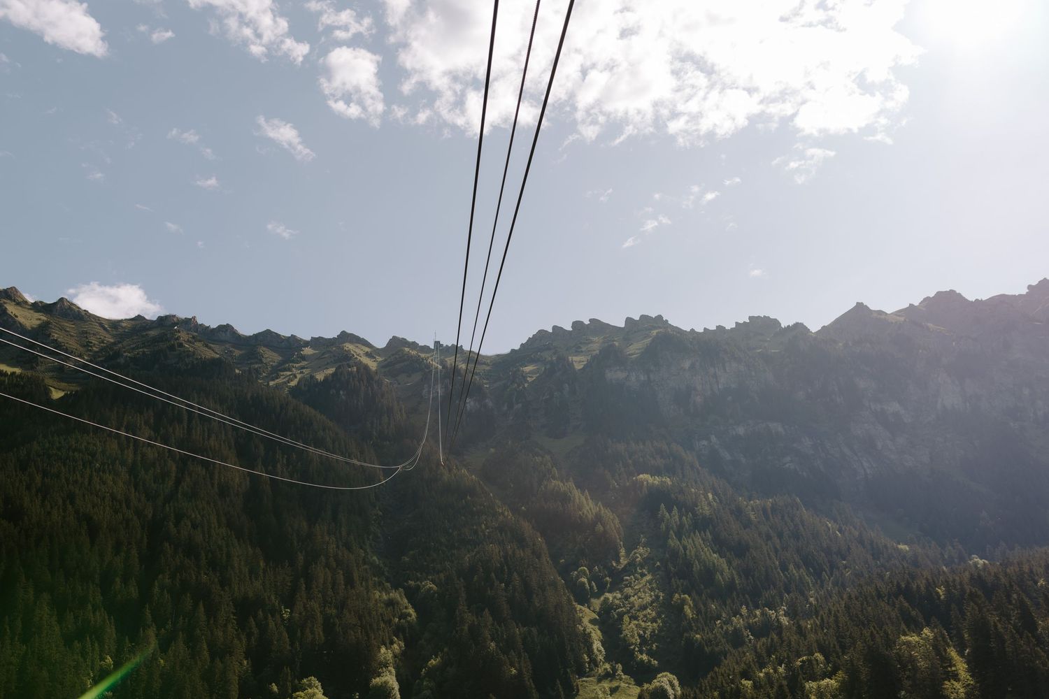Snow-capped mountain peaks under blue sky with aerial cable car lines stretching across.