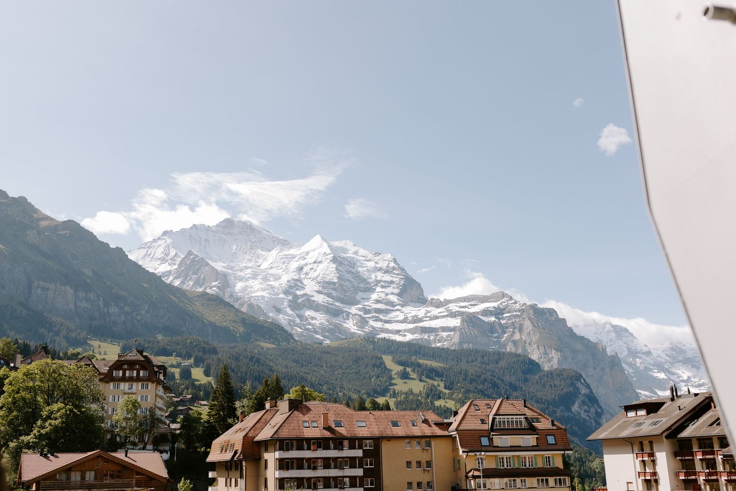 Snow-capped Alpine mountains tower over traditional Swiss village buildings.
