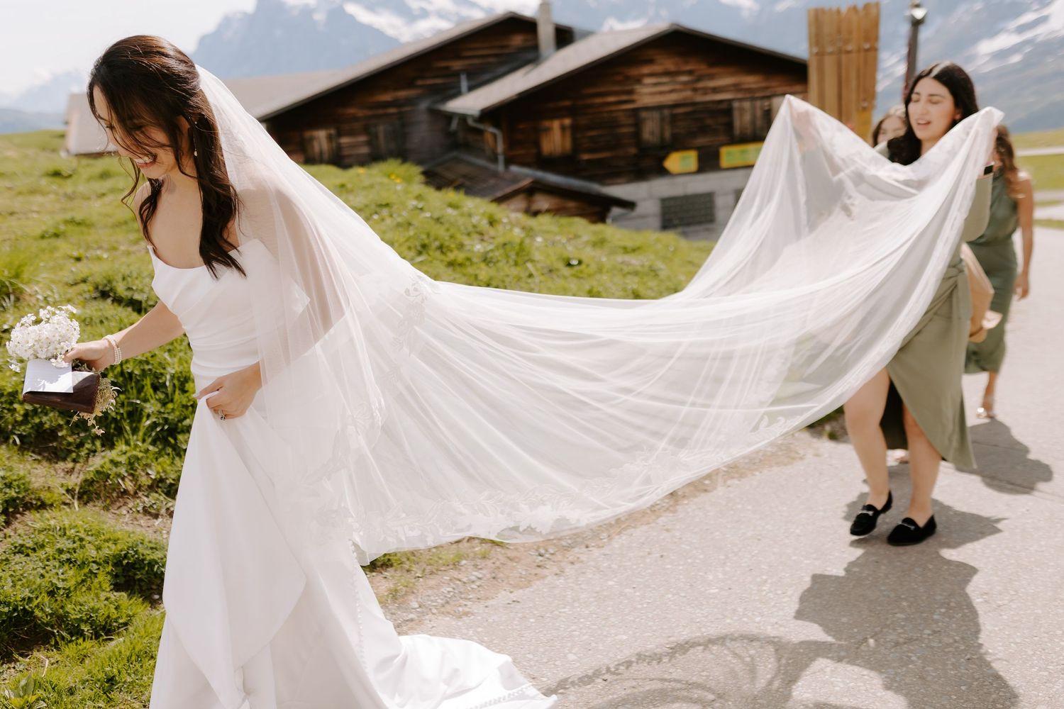 A flowing white wedding dress train spread out on an alpine path with mountains in view.