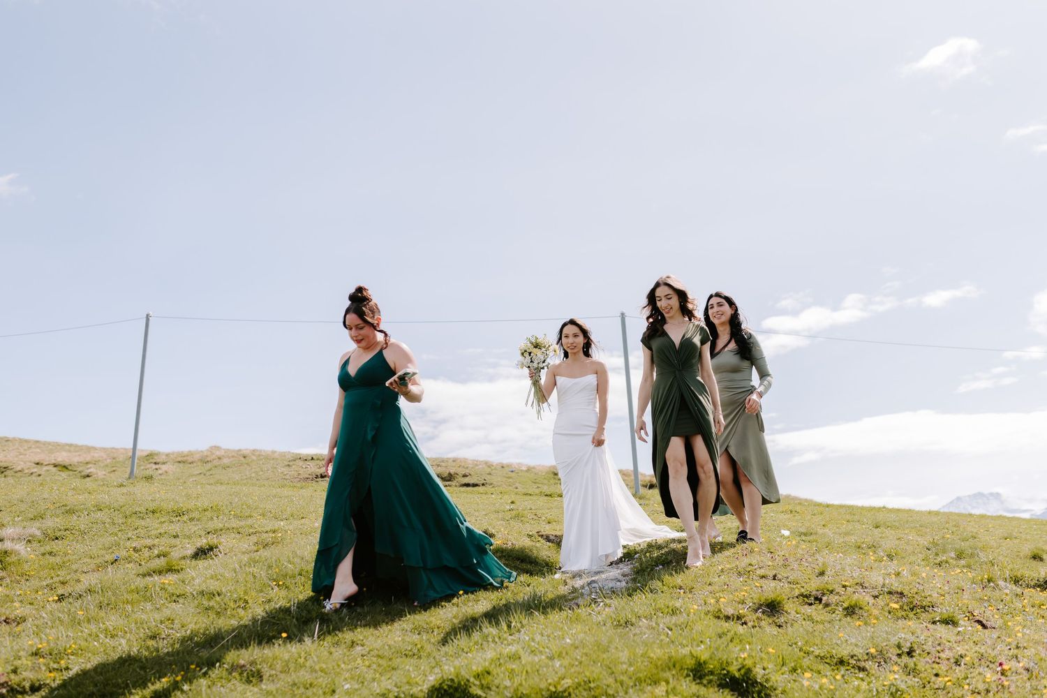 Wedding party walking through a scenic mountain meadow under bright blue skies.