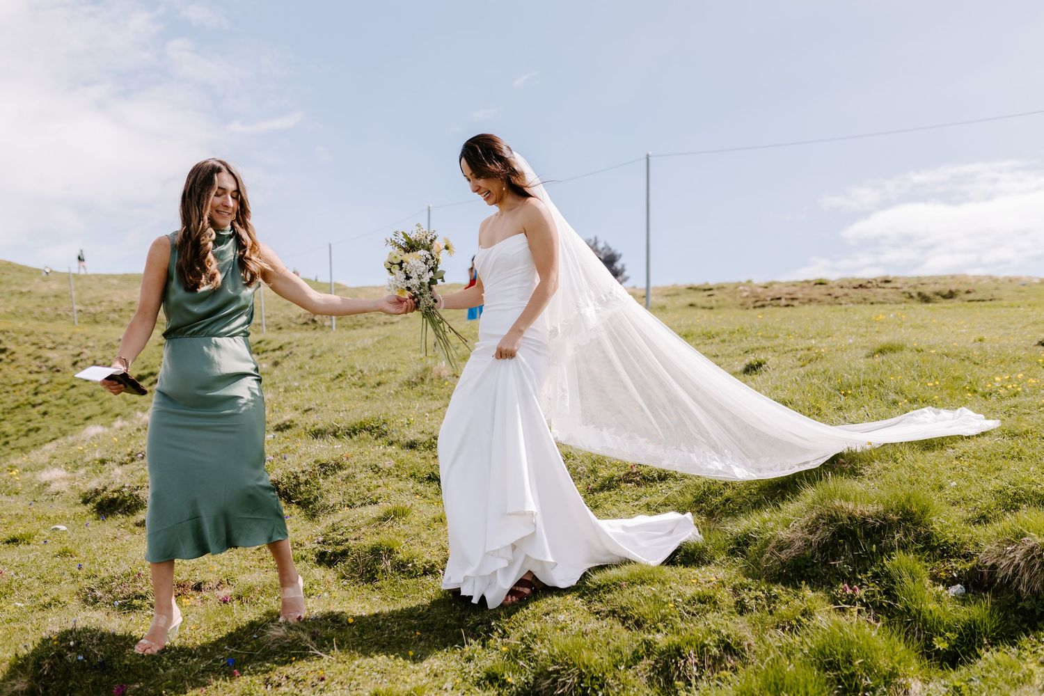 White dress flowing in mountain breeze against backdrop of green alpine meadow.