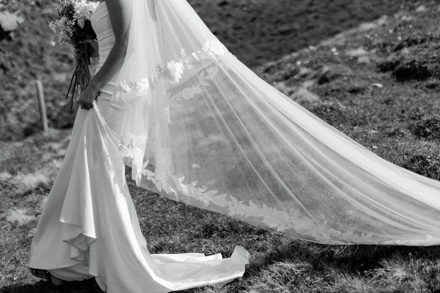 Black and white photo of a bride's flowing veil and dress silhouetted against mountain scenery.