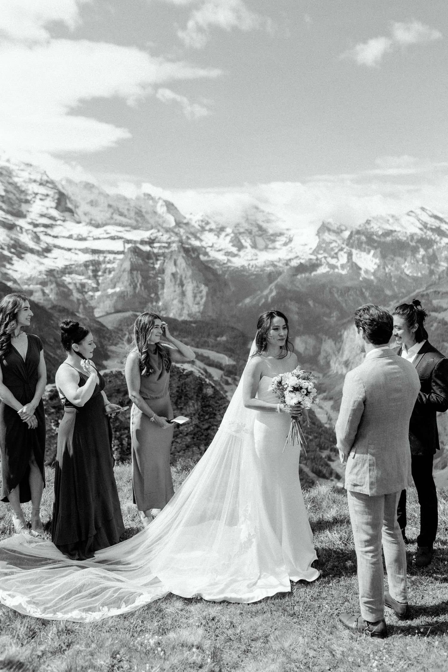 A wedding ceremony takes place in a stunning mountain landscape with snow-capped peaks in the background.