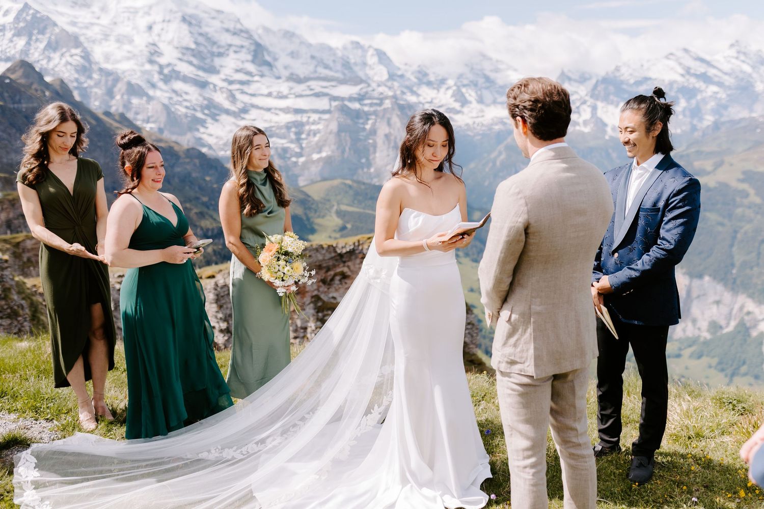 Mountain wedding ceremony with bridal party against snow-capped alpine backdrop.