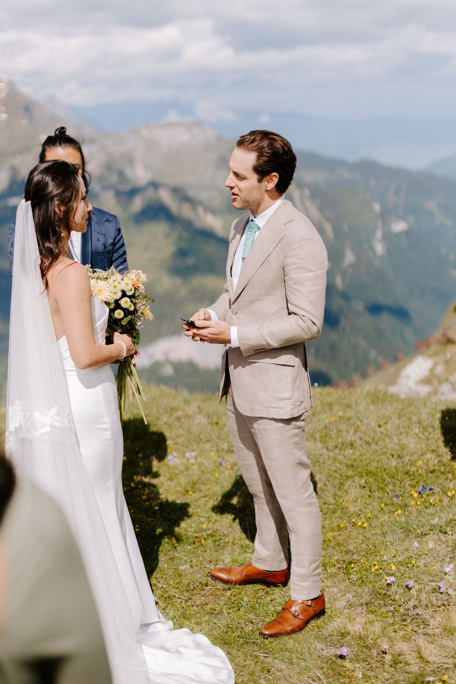 A couple exchanges wedding vows on a scenic mountain overlook with dramatic Alpine scenery behind them.