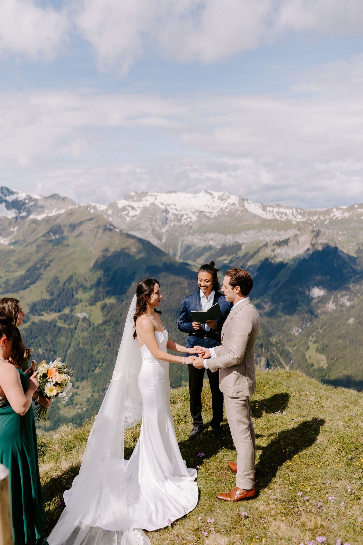 A wedding ceremony takes place against a stunning backdrop of snow-capped mountains in the Alps on a cloudy summer day.