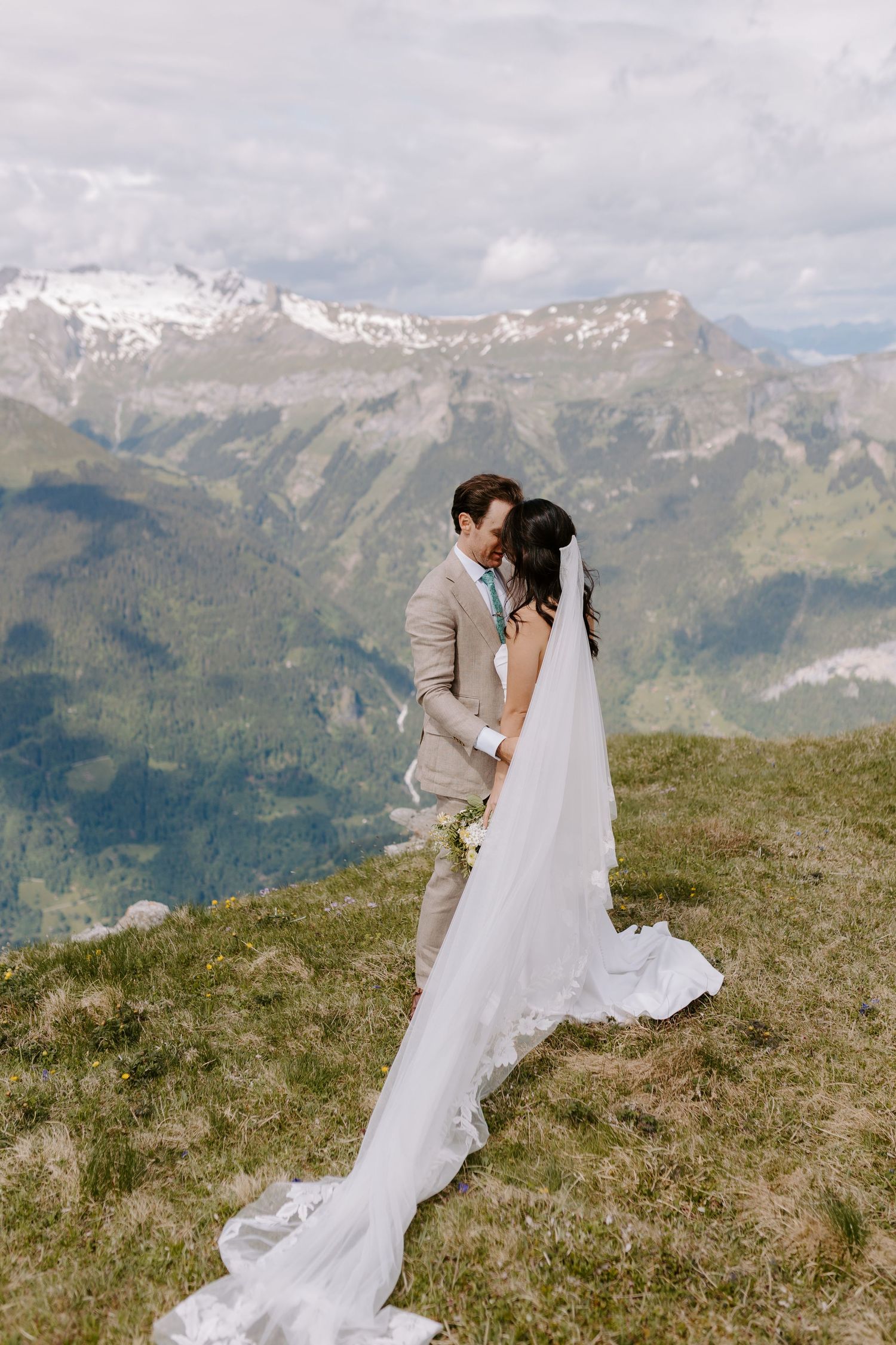 A couple embraces in their wedding attire against a stunning backdrop of snow-capped mountain peaks in the Alps.