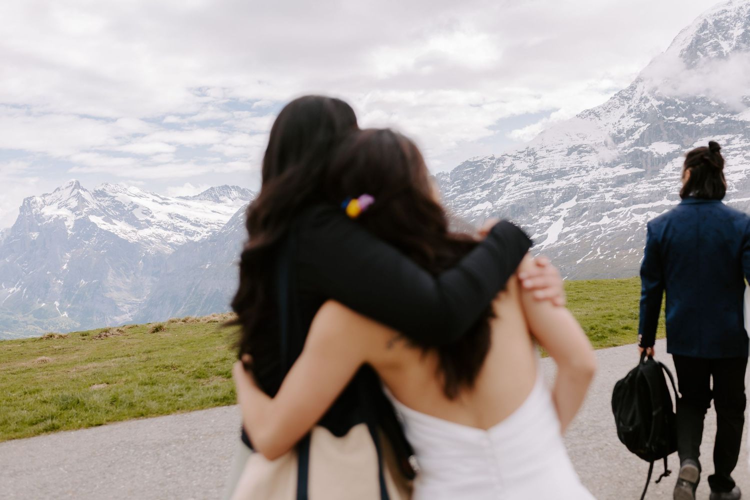 Wedding guests embrace and celebrate on a mountain summit with snow-capped peaks in the distance.