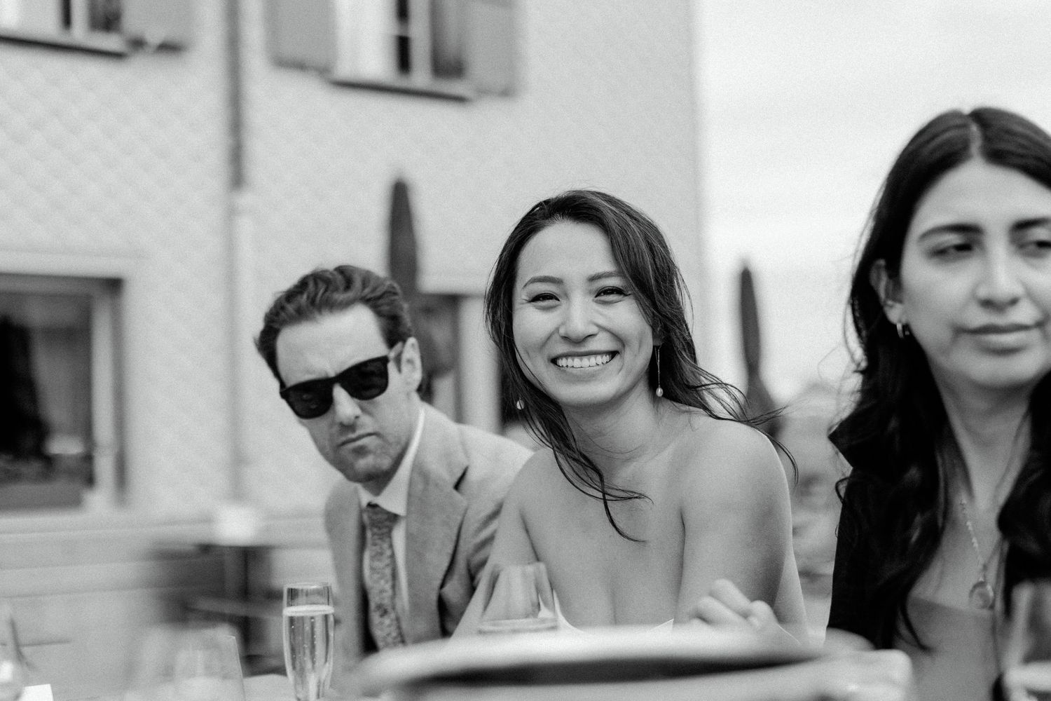 A group of wedding guests enjoying drinks and conversation at an outdoor table.