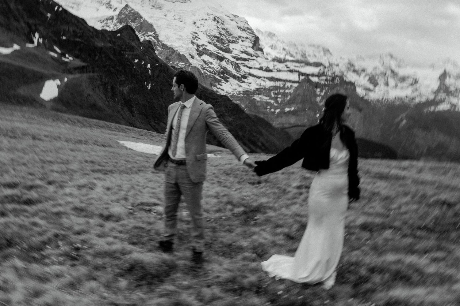 A couple celebrates their wedding against a dramatic mountain backdrop with snow-capped peaks in the distance.