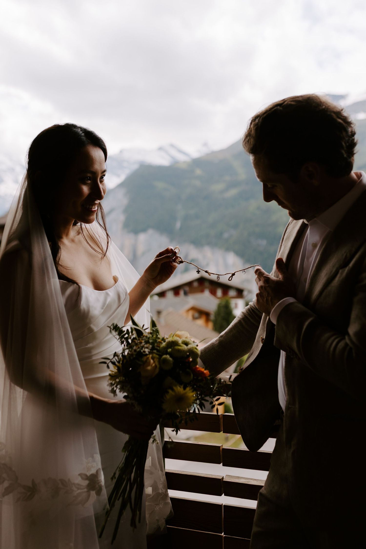 Silhouettes in a wedding dress and suit interact with dramatic mountain scenery behind them.