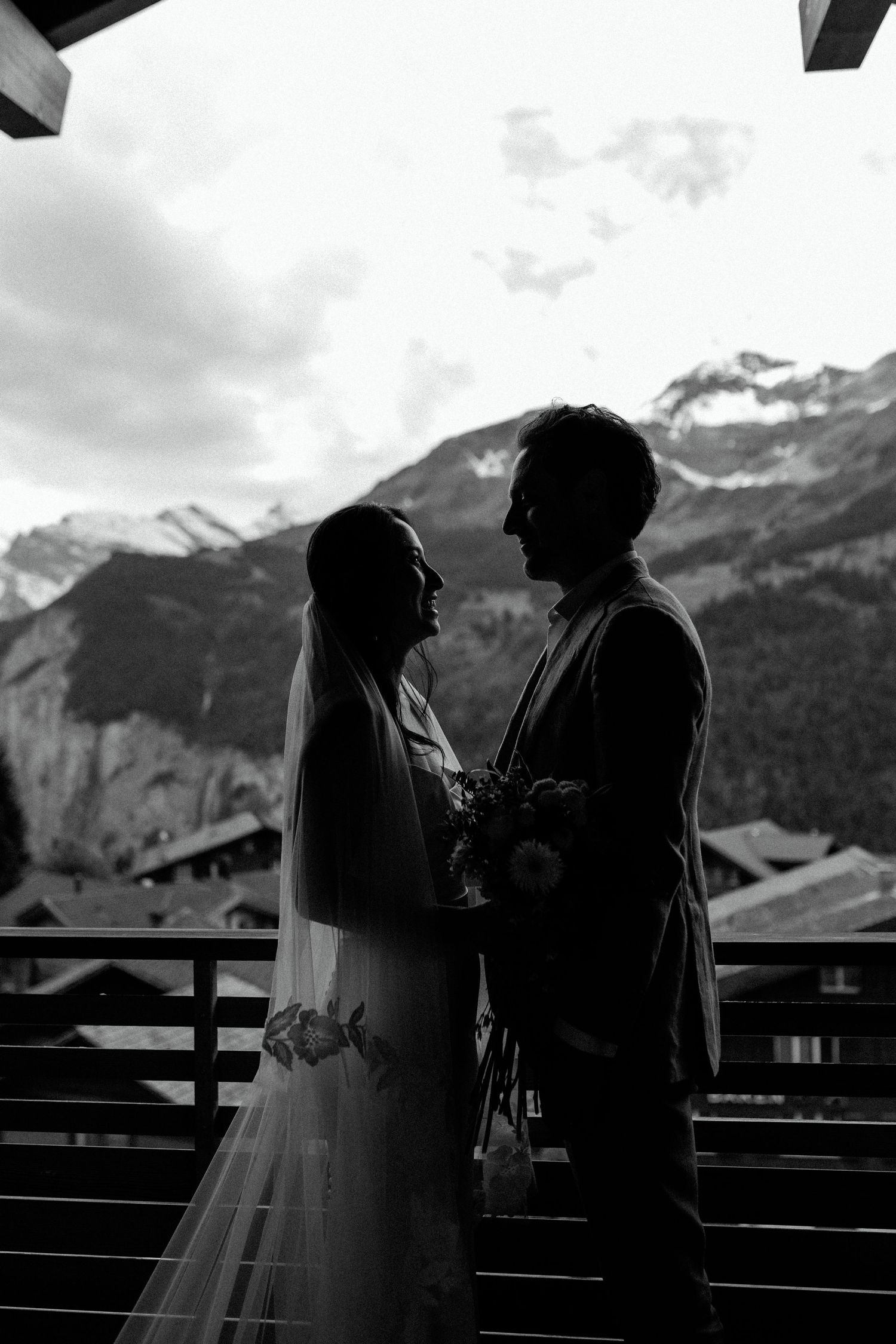Dramatic silhouette of two people sharing an intimate moment on a balcony with mountain views.