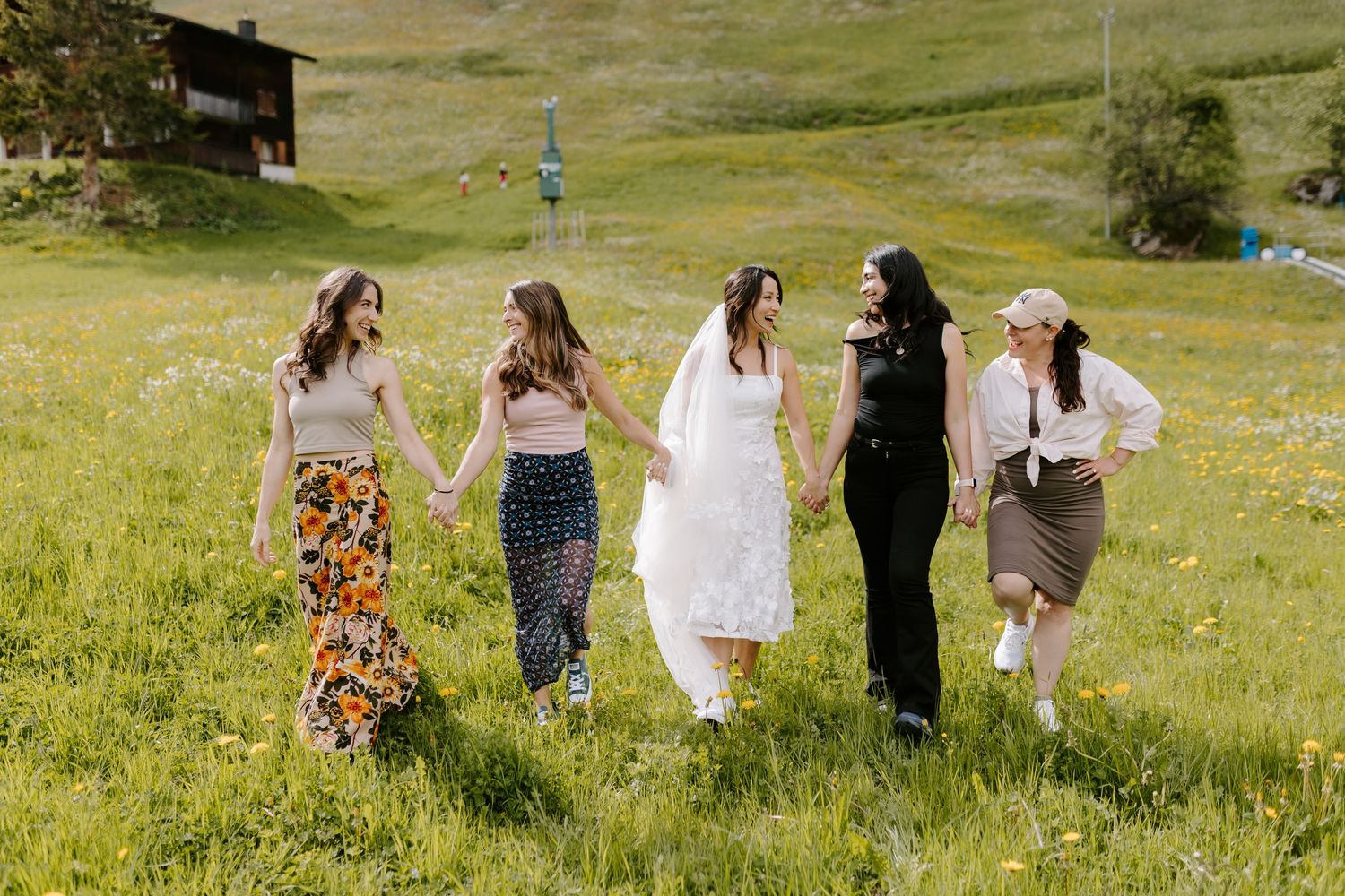 Group of friends in colorful dresses walking through green mountain meadow.