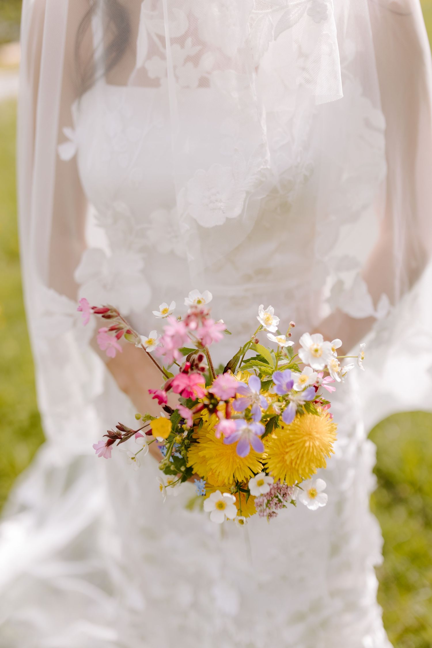 Close-up of a bridal bouquet featuring yellow dandelions and white daisies against a white dress.