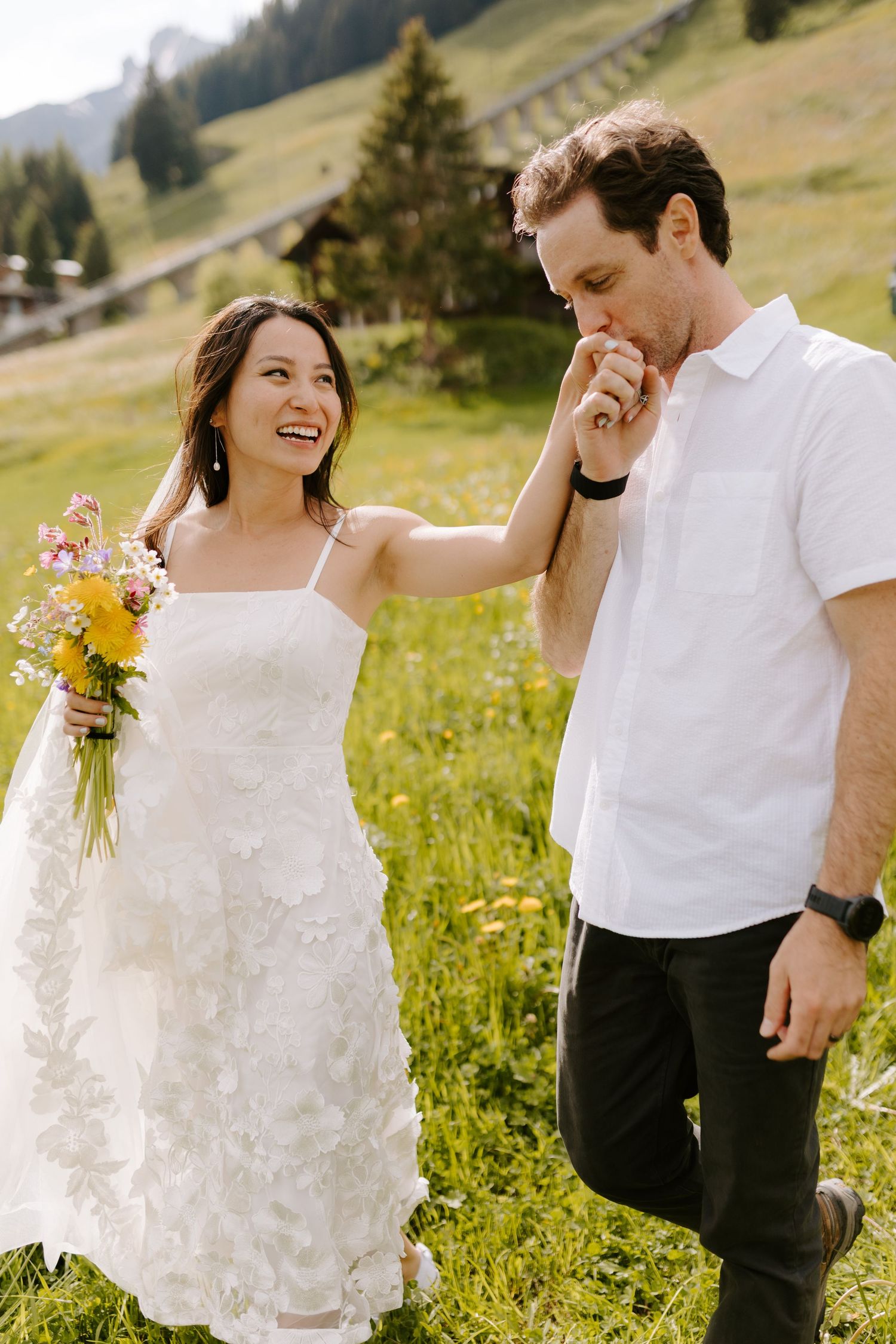 A couple share joyful moments together in a meadow of wildflowers against a mountainous landscape.