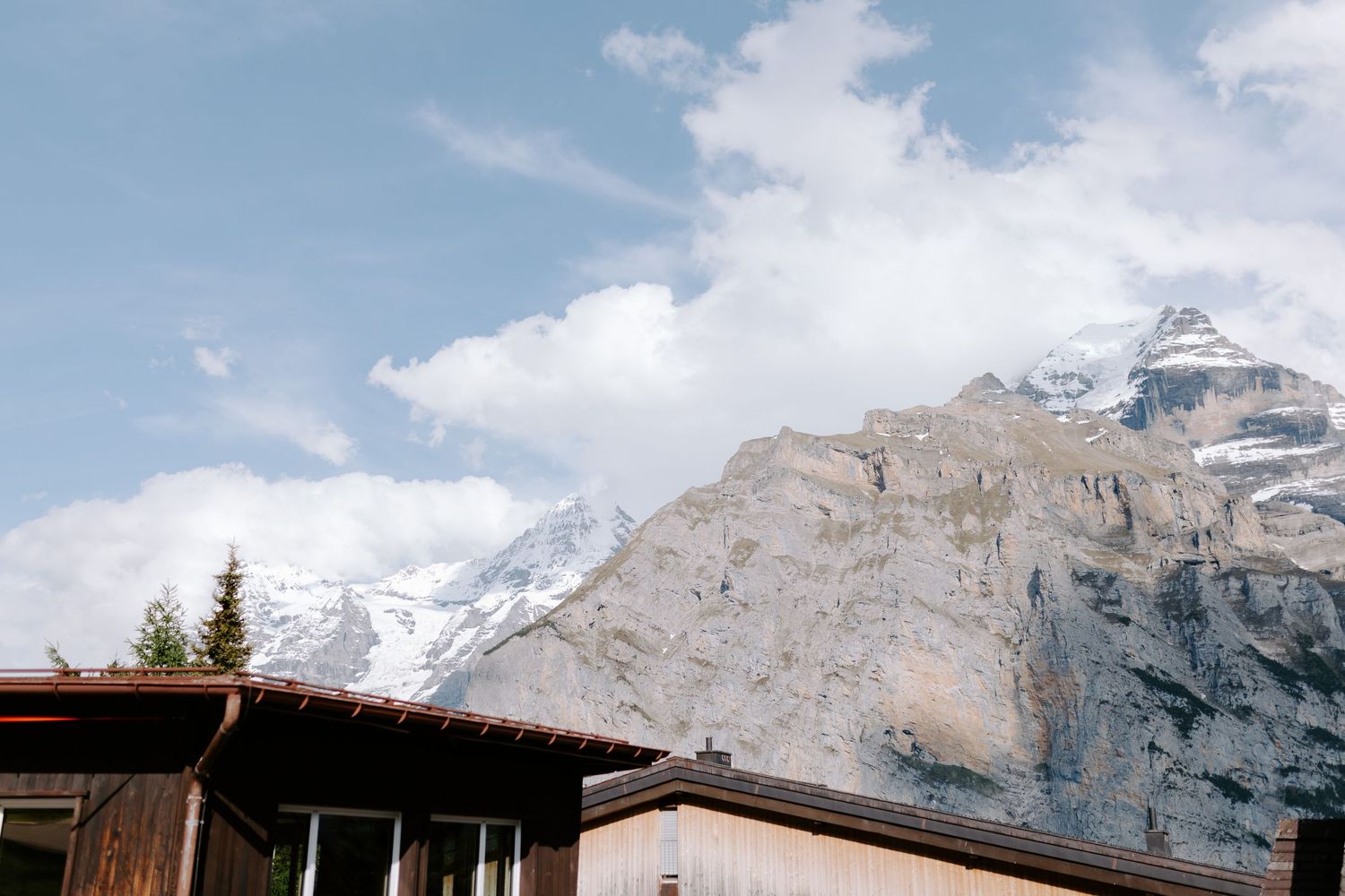 Snow-capped mountain peaks rising above wooden buildings under blue sky.