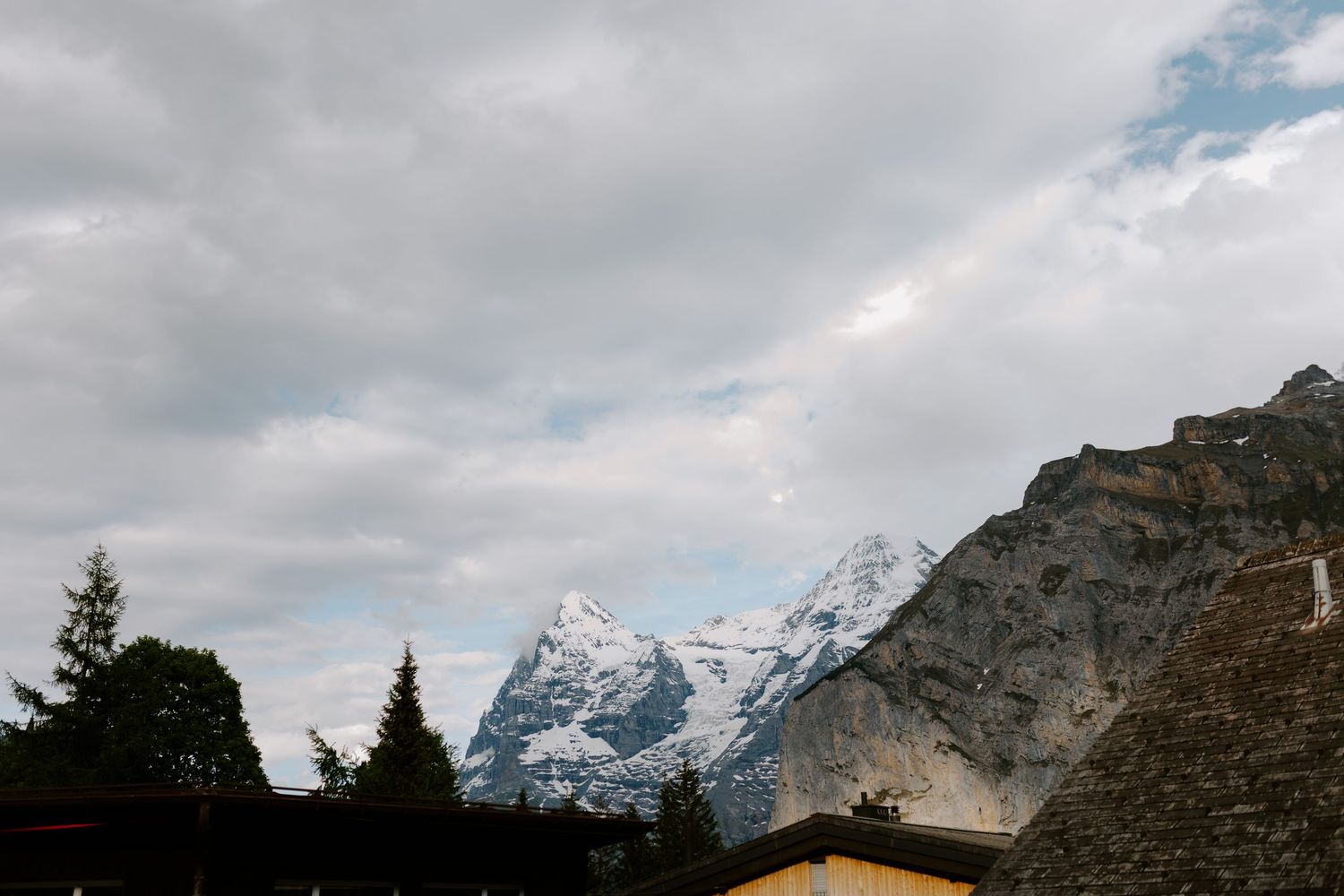 Snow-capped mountain peaks rise against a cloudy sky in a dramatic alpine landscape.