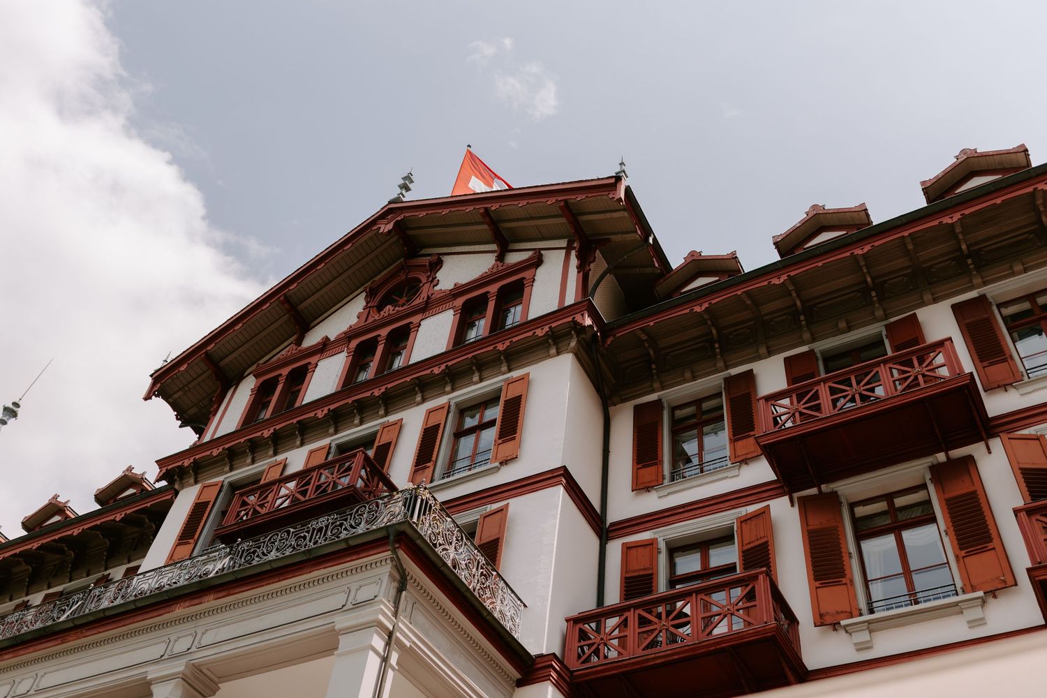 Traditional Swiss hotel building with red balconies and ornate architecture against cloudy sky.
