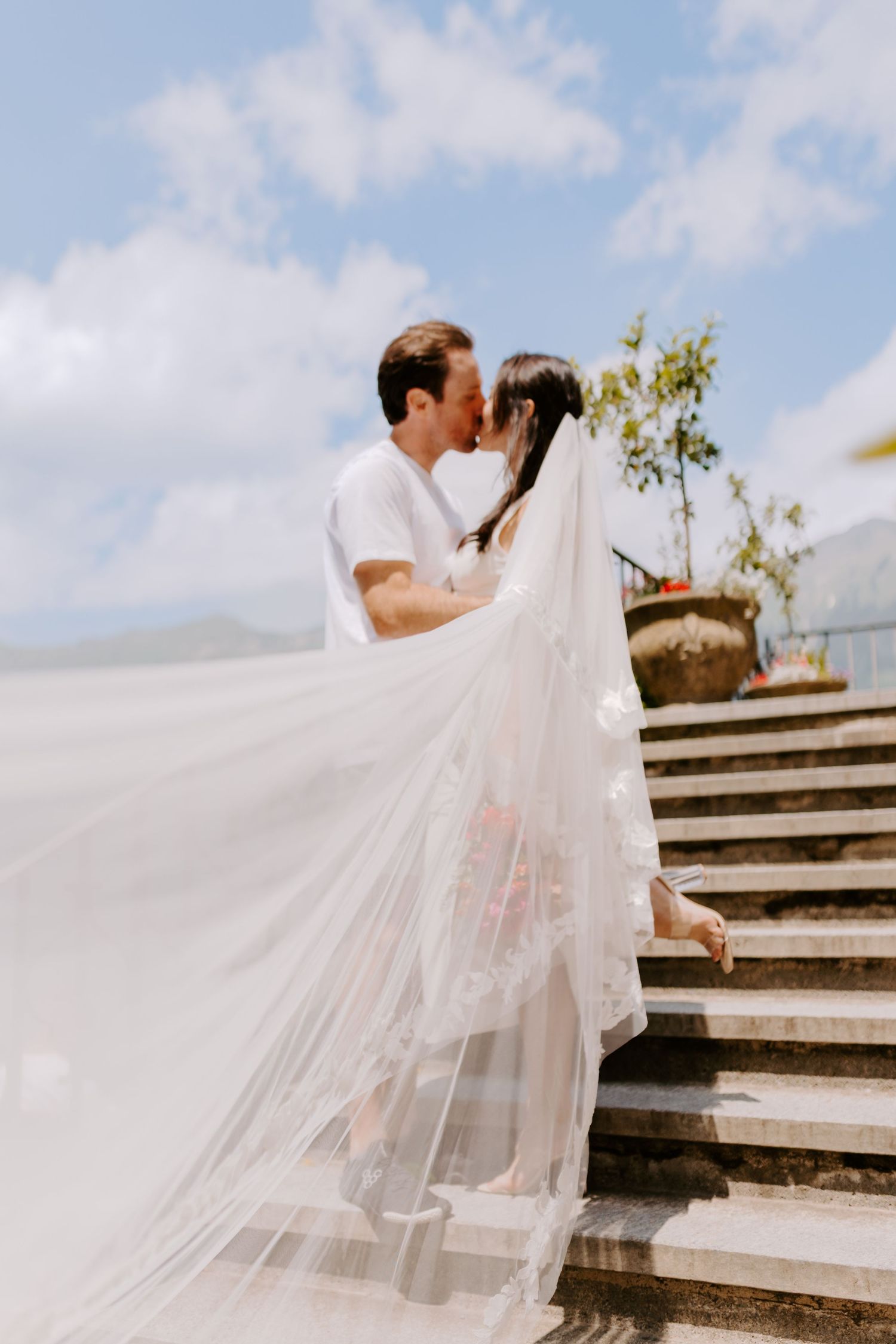 A romantic moment captured on stone stairs with flowing white veil in the breeze.