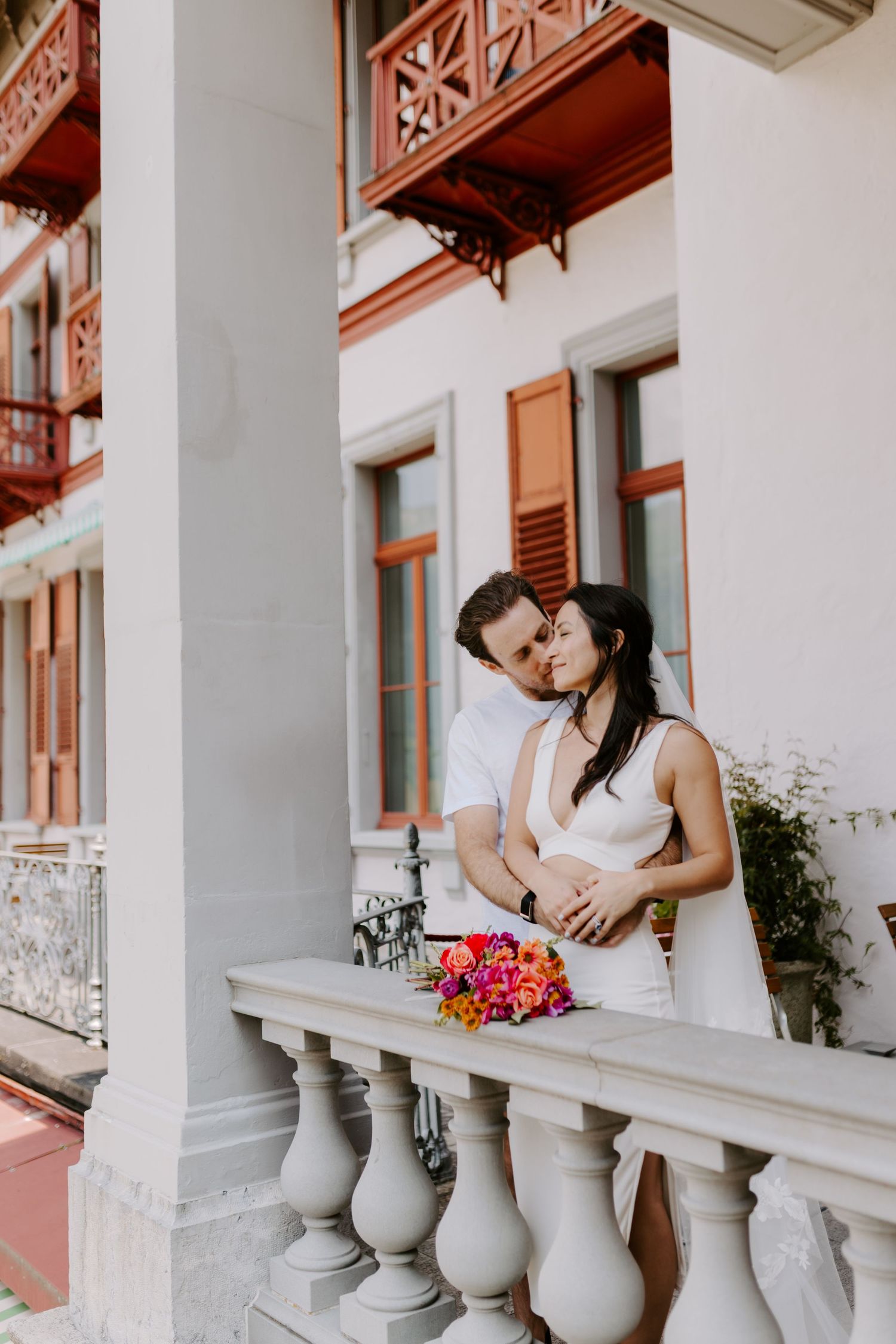 A romantic moment shared on an elegant white balcony with ornate stone railings.
