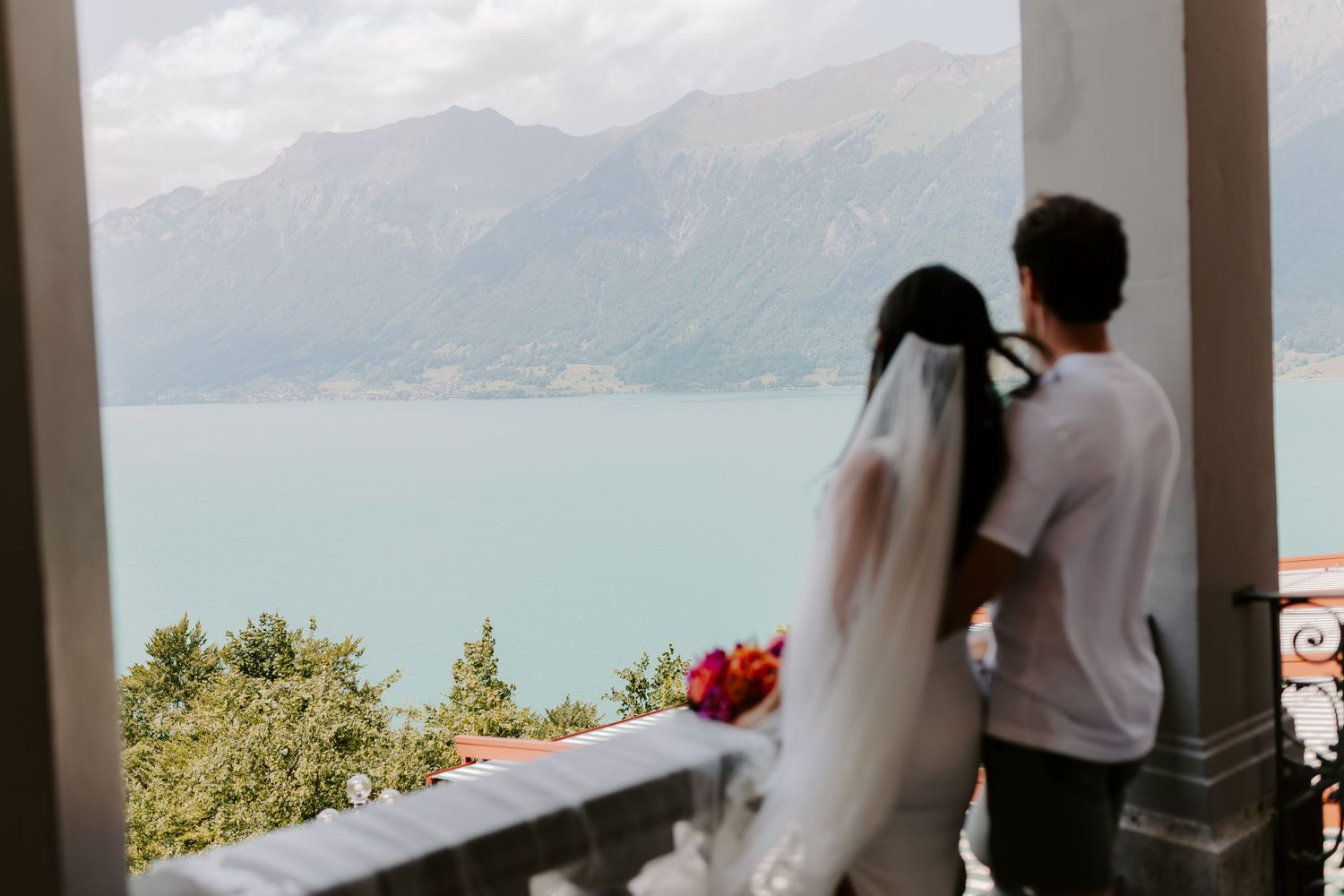 A couple shares an intimate moment on a balcony overlooking a scenic mountain lake view.