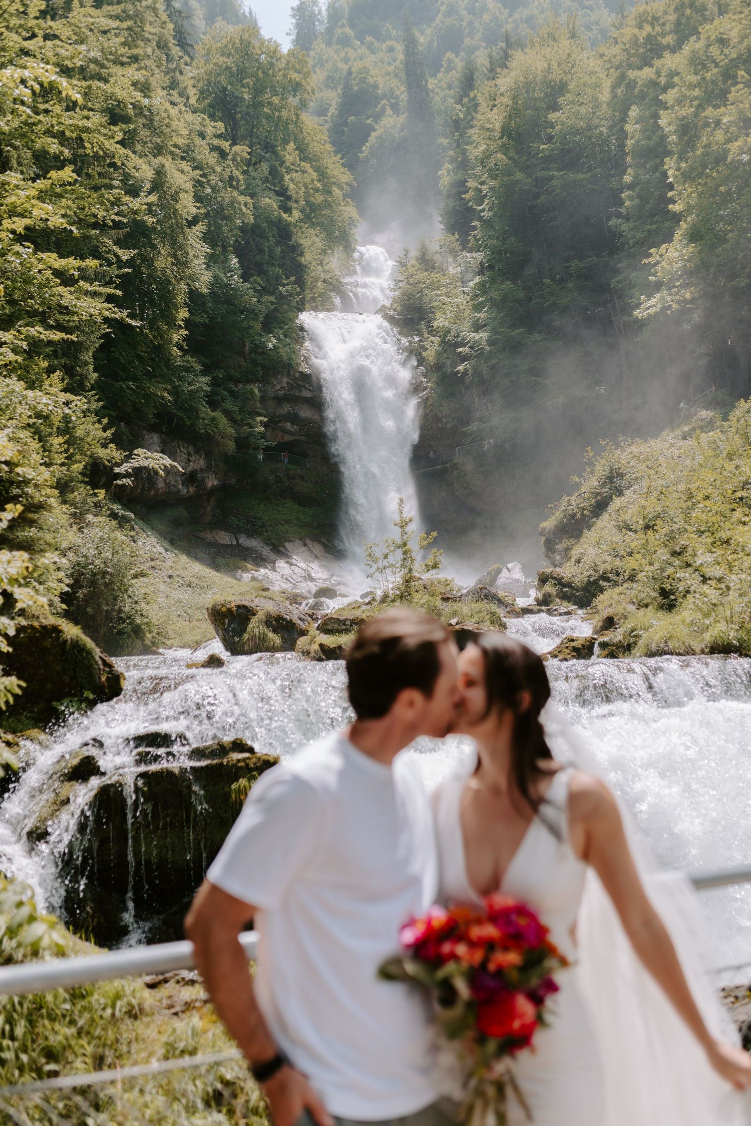 A couple shares an intimate moment in front of a majestic forest waterfall.