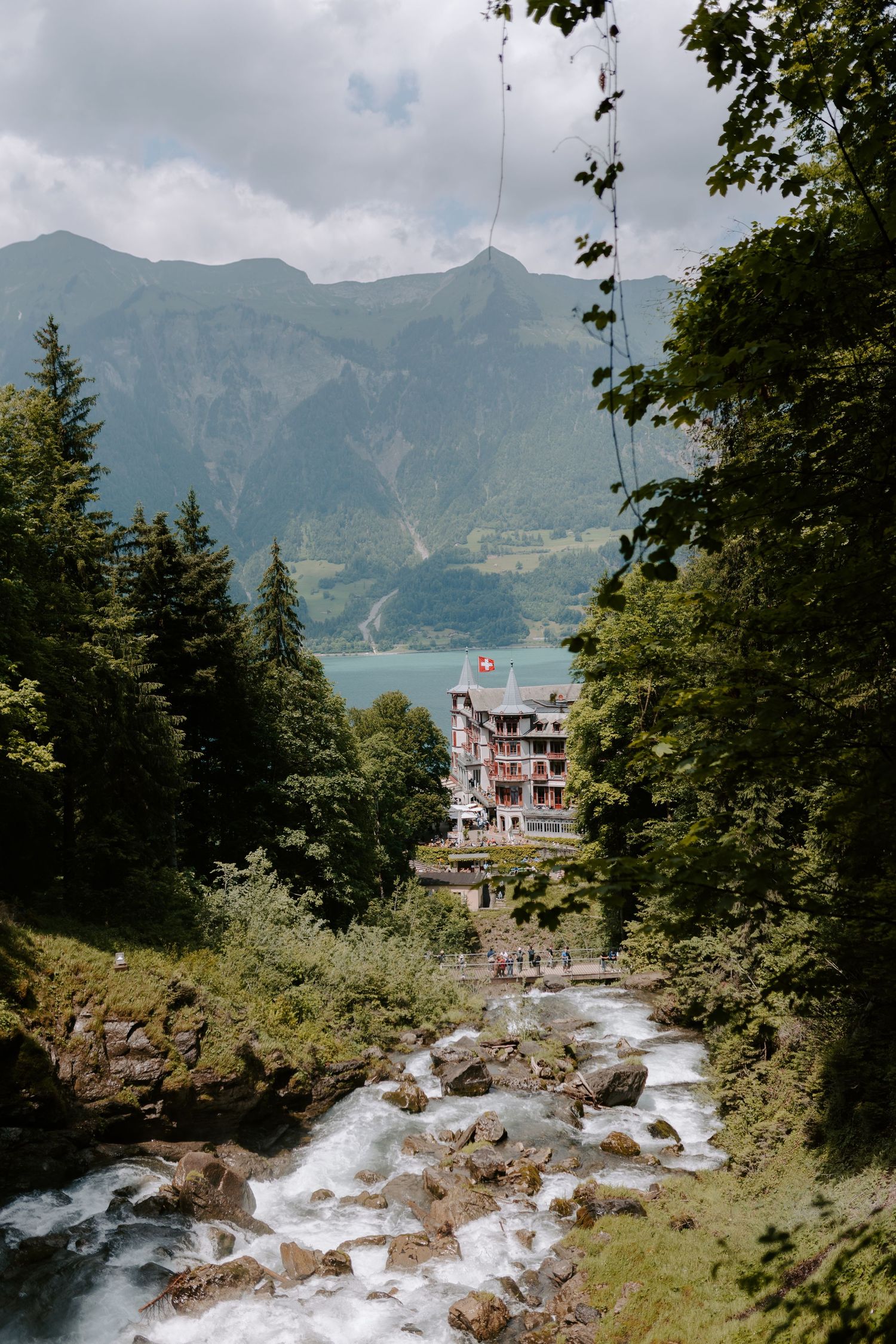 A scenic mountain landscape with rushing stream and historic hotel nestled among green forests.