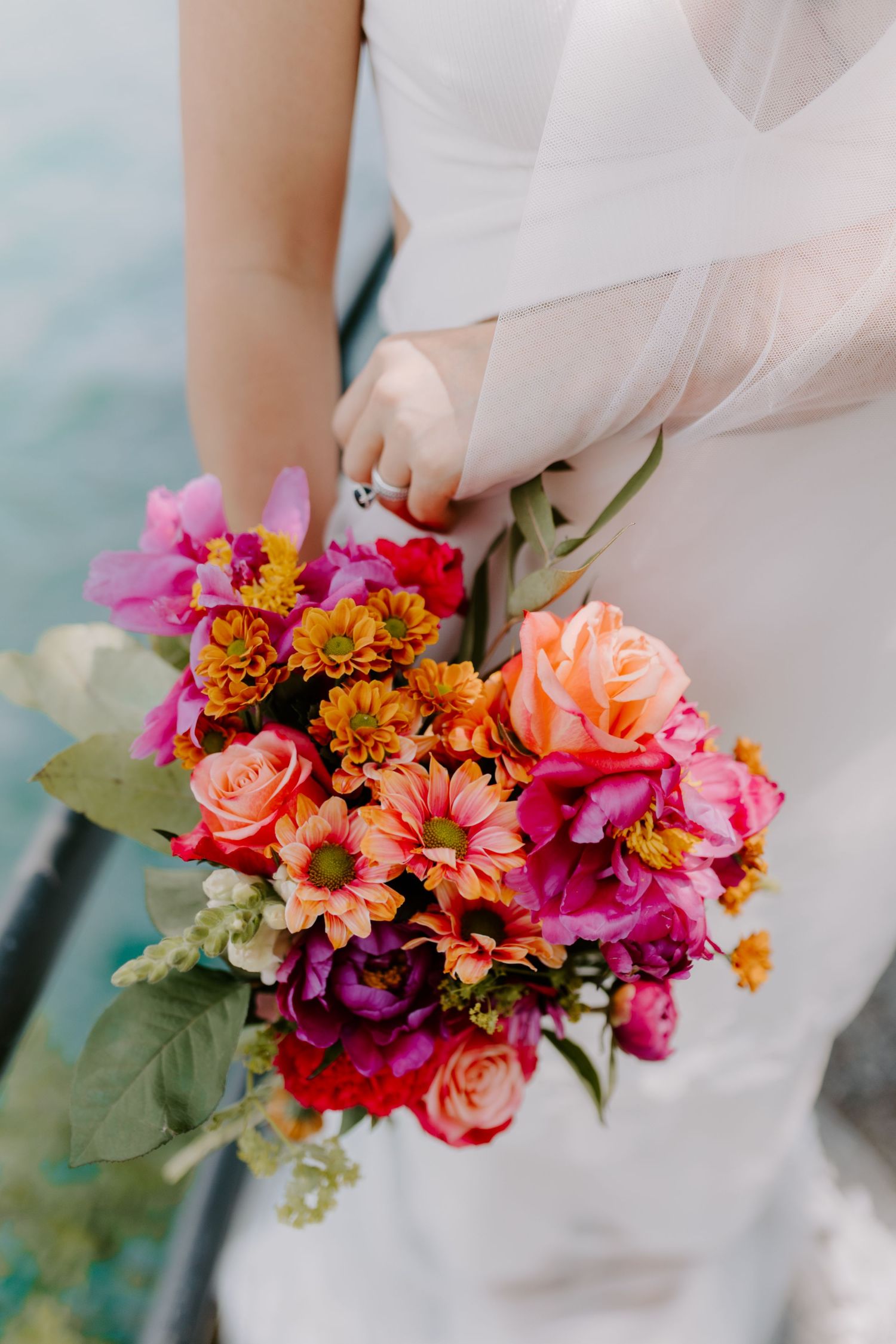 Vibrant bridal bouquet featuring pink, orange, and coral flowers against a white wedding dress.