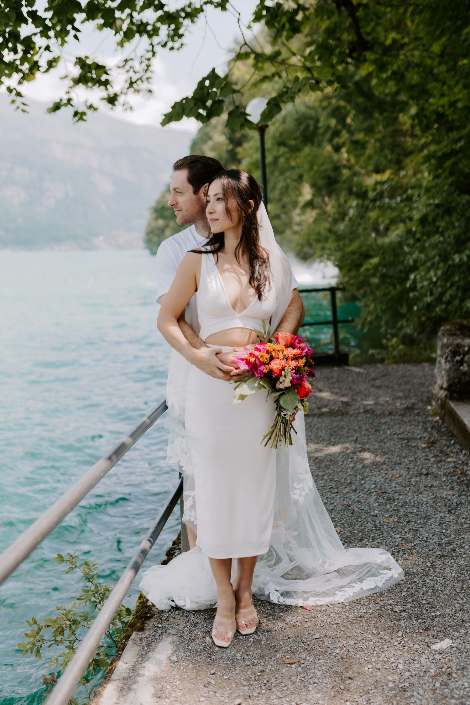 A couple poses for a romantic portrait on a lakeside path with colorful flowers.