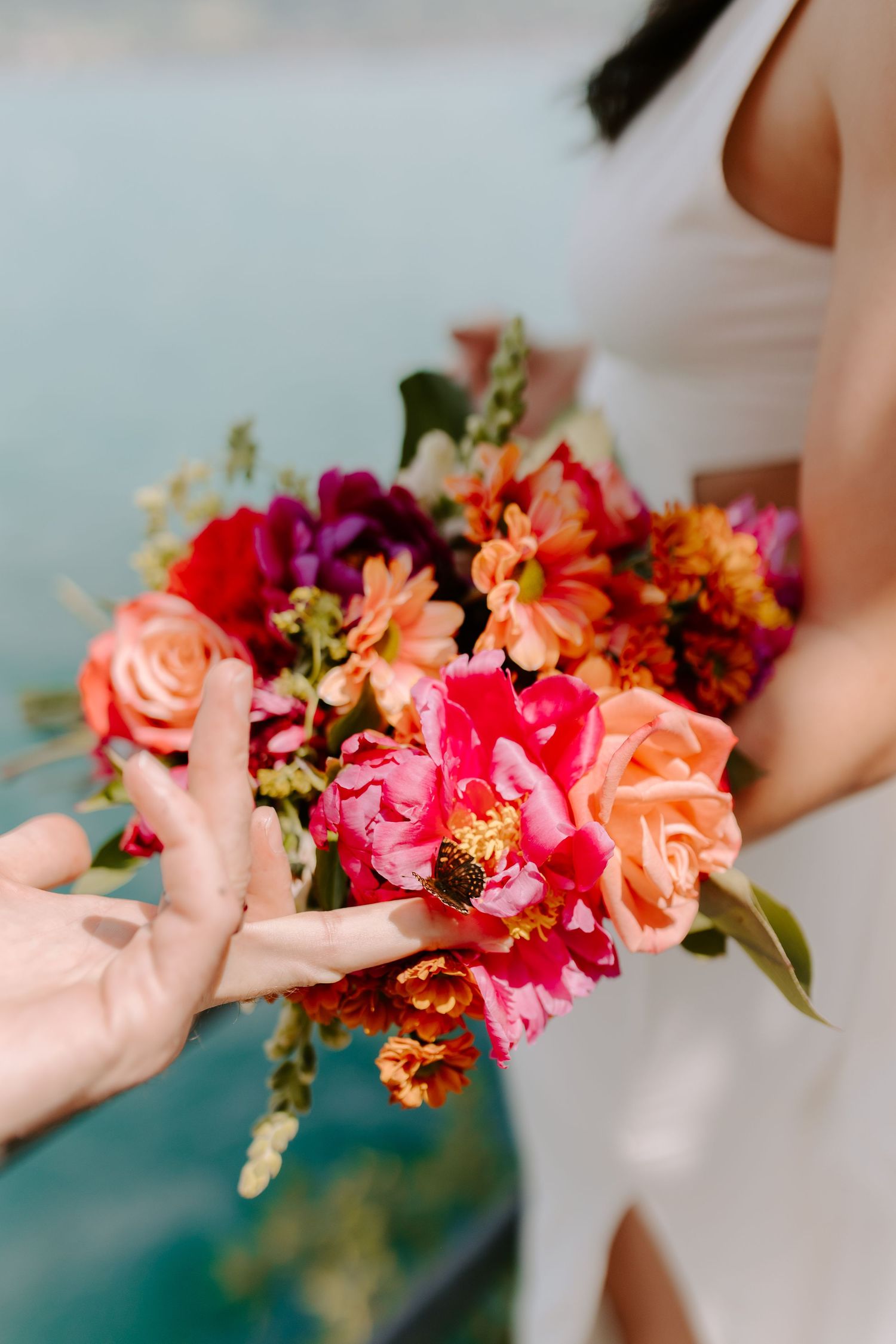 Vibrant bouquet with pink, orange, and red flowers being passed between hands.
