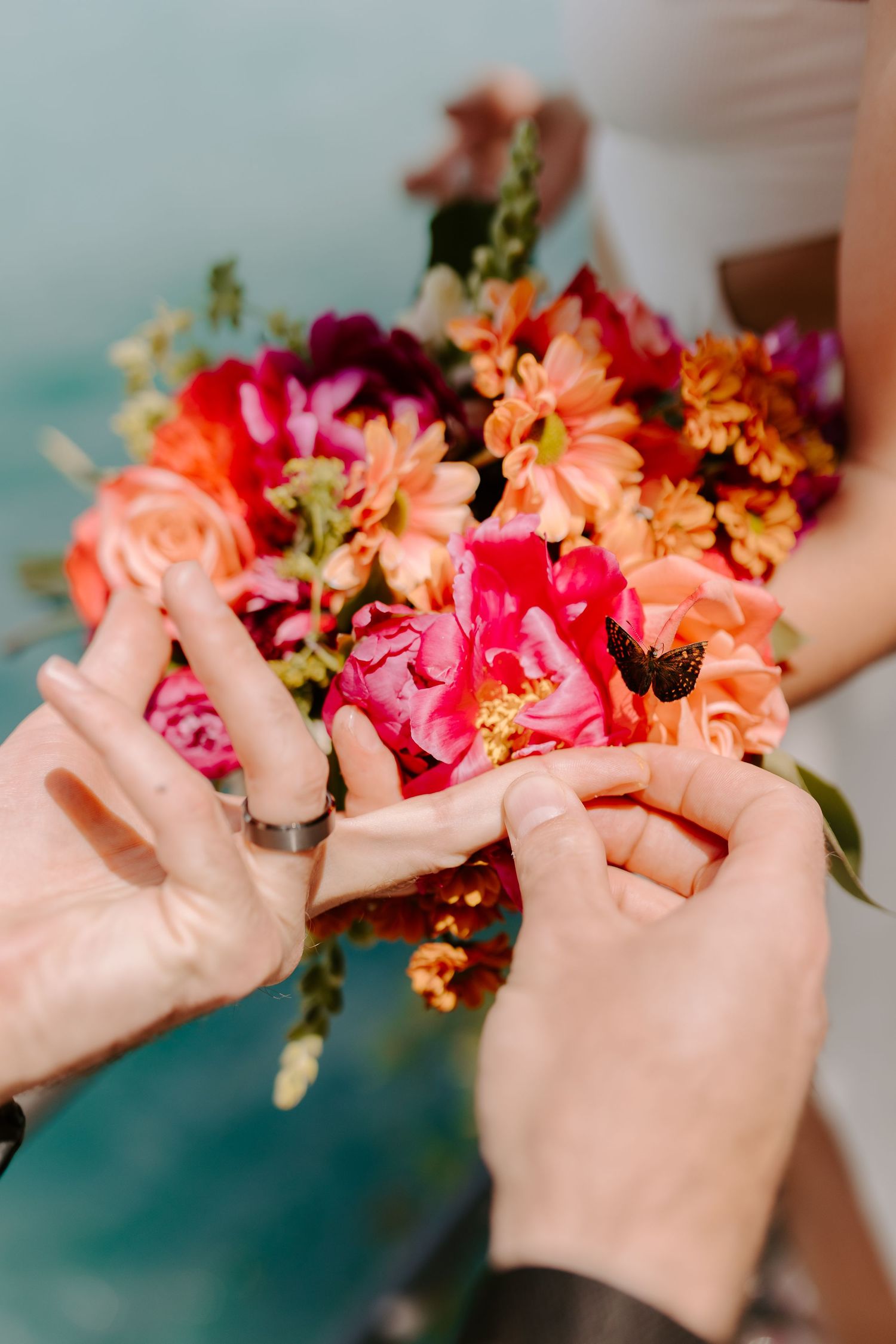 Hands arranging a vibrant bouquet of coral, pink and peach flowers against a turquoise background.