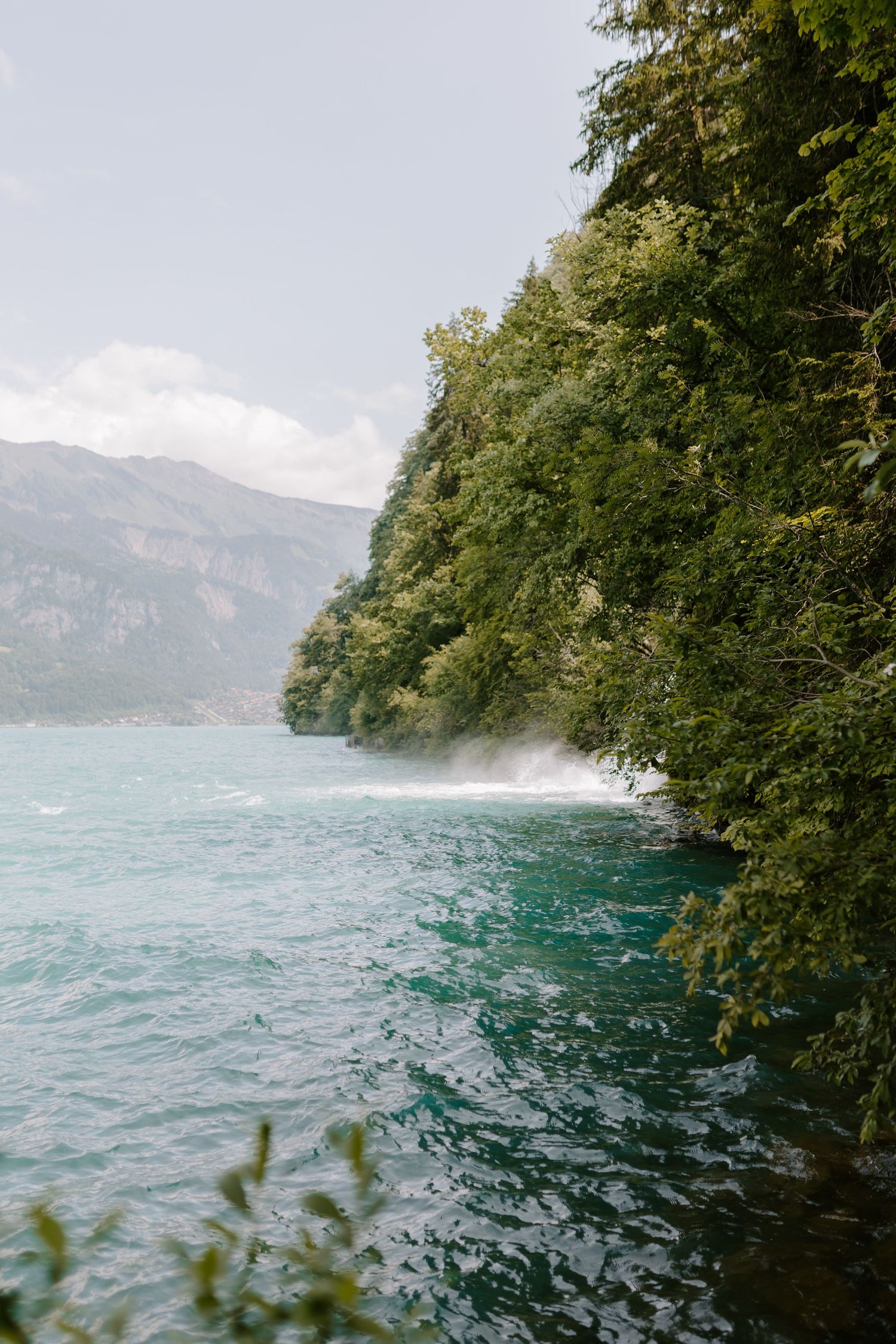 Turquoise waters meet forested cliffs at a dramatic mountain lake with waves crashing against the shoreline.