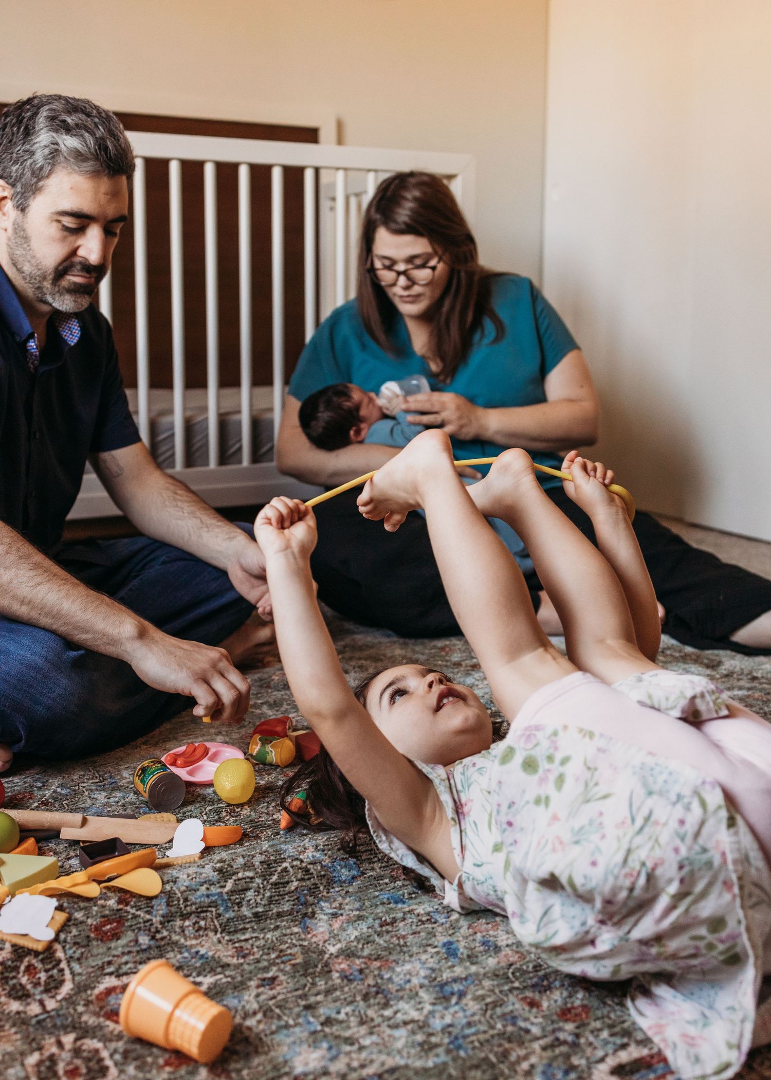 Healthcare provider examines a baby on a play mat while another caregiver looks on during a home visit.