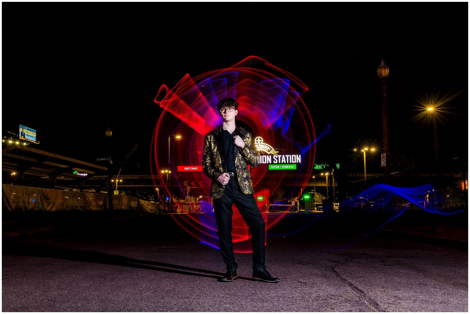 Long exposure night photograph shows light painting creating glowing red and blue spiral patterns against dark urban backdrop.
