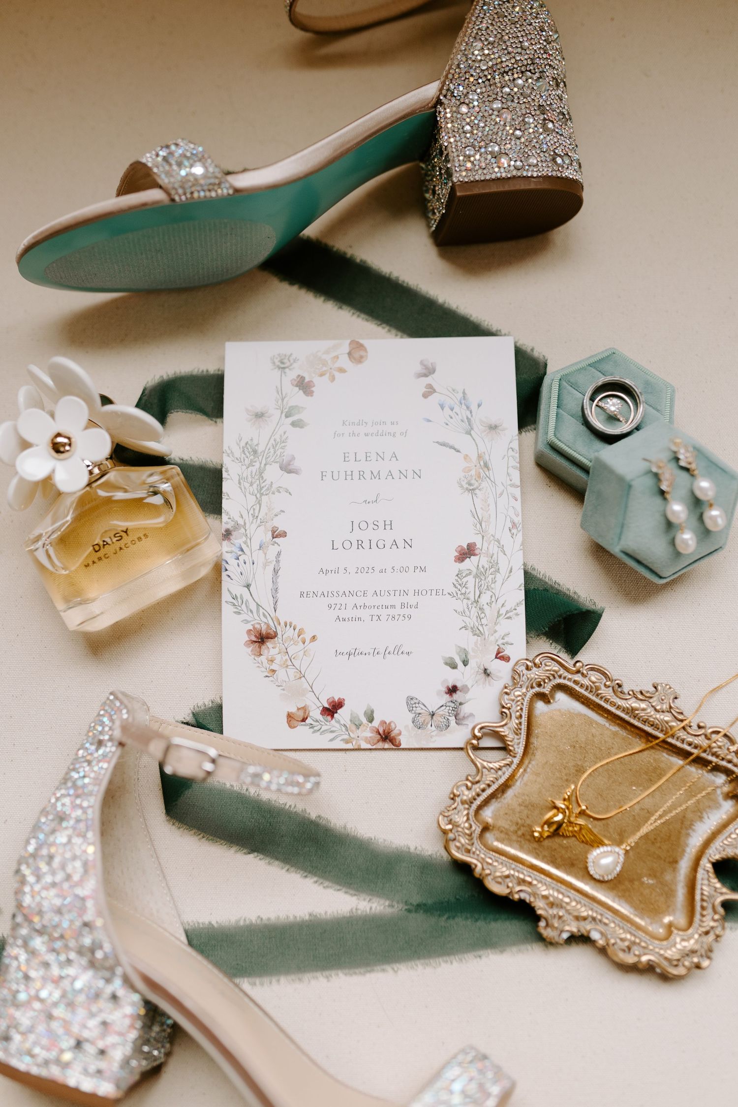 Wedding details flatlay with sparkly shoes, floral invitation, perfume bottle, and ring box in mint and gold tones.